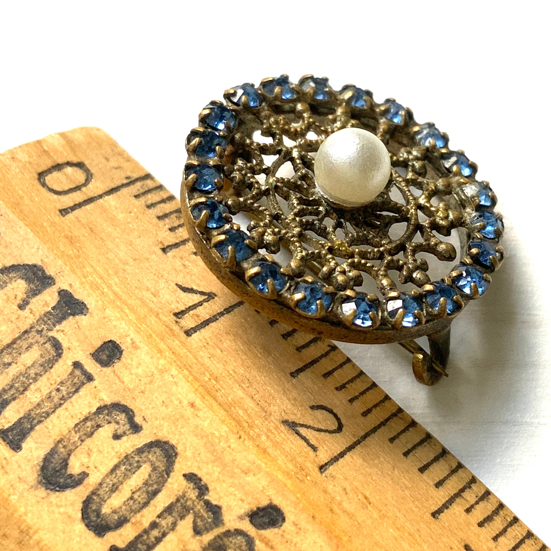 This petite brooch features a delicate round gold-tone filigree, crowned with a small glass pearl. 繊細なラウンドのゴールドトーン フィリグリーに、グラスパールがちょこんと乗ったミニブローチ。