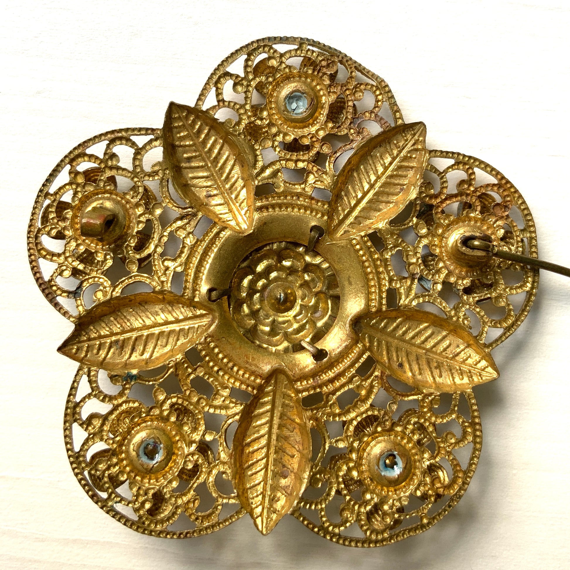 This brooch features a gold-tone floral filigree design, delicately painted with soft blue enamel flowers.  ゴールドトーンのお花の形のフィリグリーに、淡いブルーでエナメルペイントされたお花が描かれたブローチ。