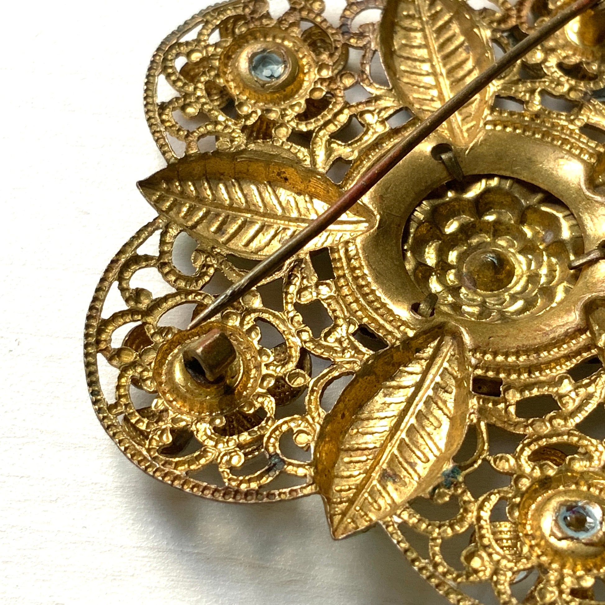 This brooch features a gold-tone floral filigree design, delicately painted with soft blue enamel flowers.  ゴールドトーンのお花の形のフィリグリーに、淡いブルーでエナメルペイントされたお花が描かれたブローチ。
