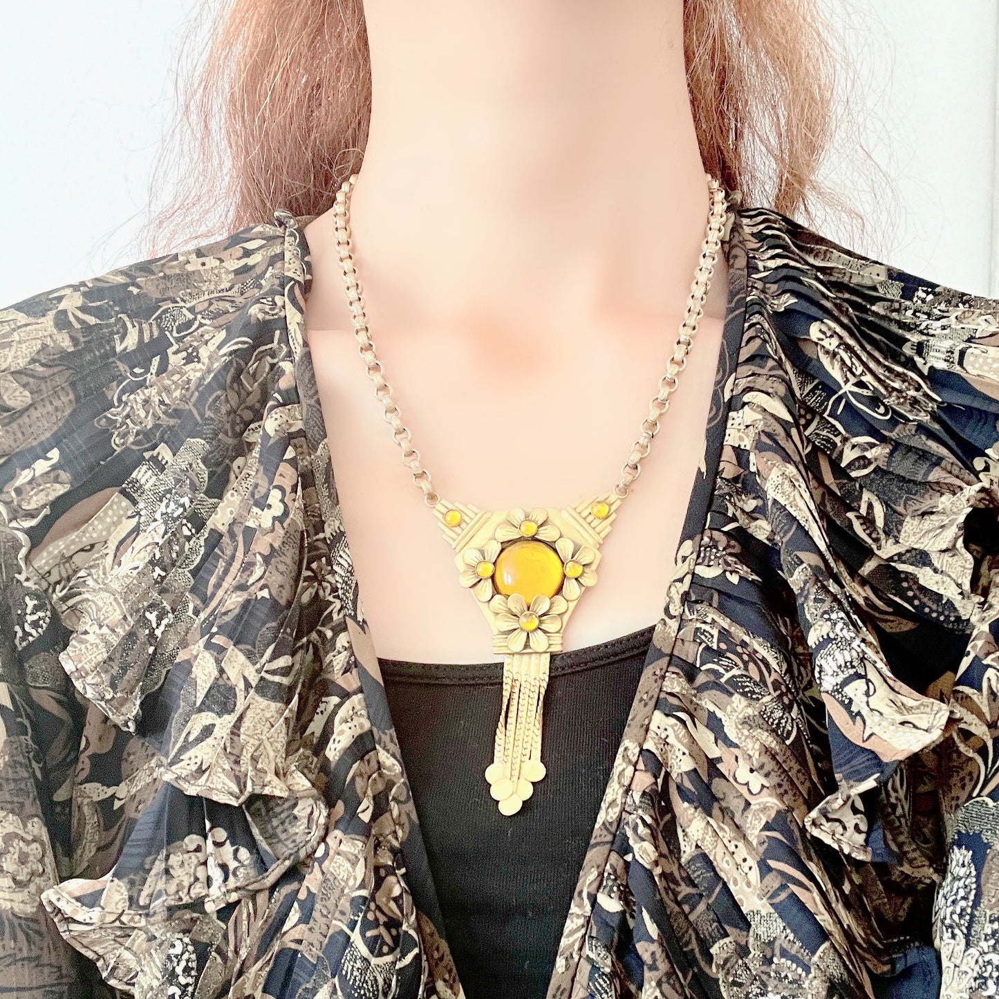 A bright orange cabochon glass, like a little sun, is surrounded by gold-tone metal flowers in this stunning necklace. お日様のように明るいオレンジのカボショングラスを、ゴールドトーンメタルのお花がぐるりと囲んだネックレス。