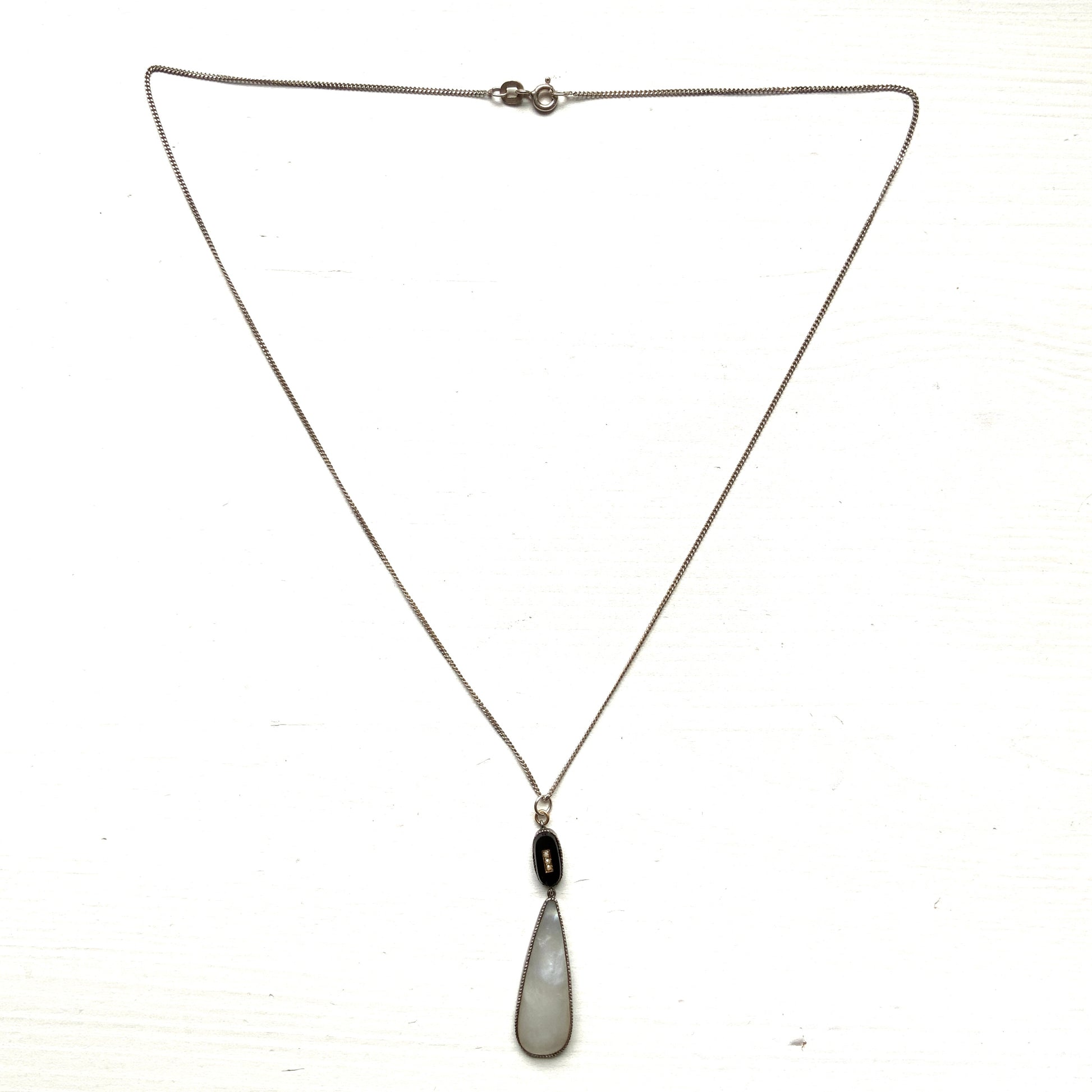 A silver necklace featuring onyx-like black glass paired with a teardrop of smooth, lustrous mother of pearl. オニキスのような艶をもつブラックグラスと、滑らかな光沢が美しいマザーオブパールのティアドロップを組み合わせた、シルバーネックレス。