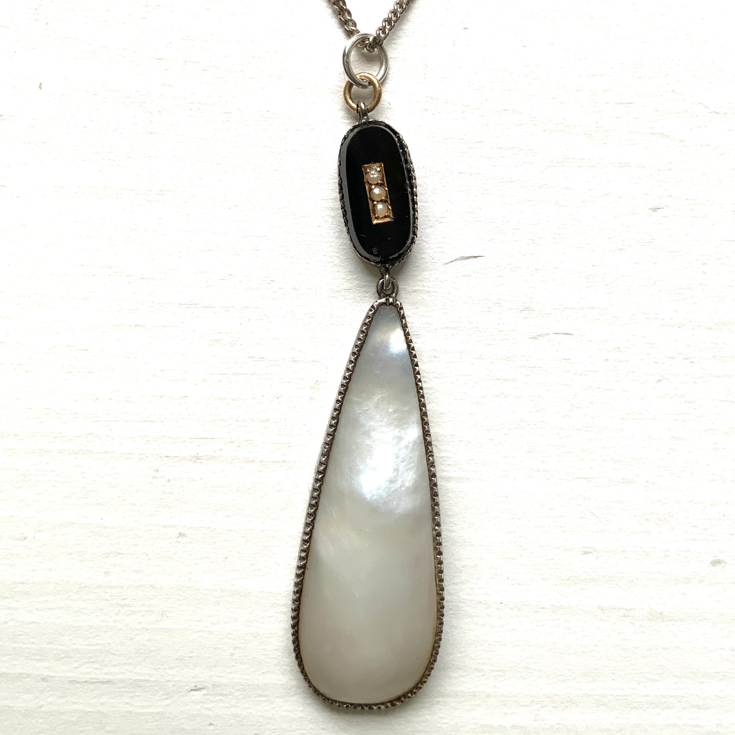 A silver necklace featuring onyx-like black glass paired with a teardrop of smooth, lustrous mother of pearl. オニキスのような艶をもつブラックグラスと、滑らかな光沢が美しいマザーオブパールのティアドロップを組み合わせた、シルバーネックレス。