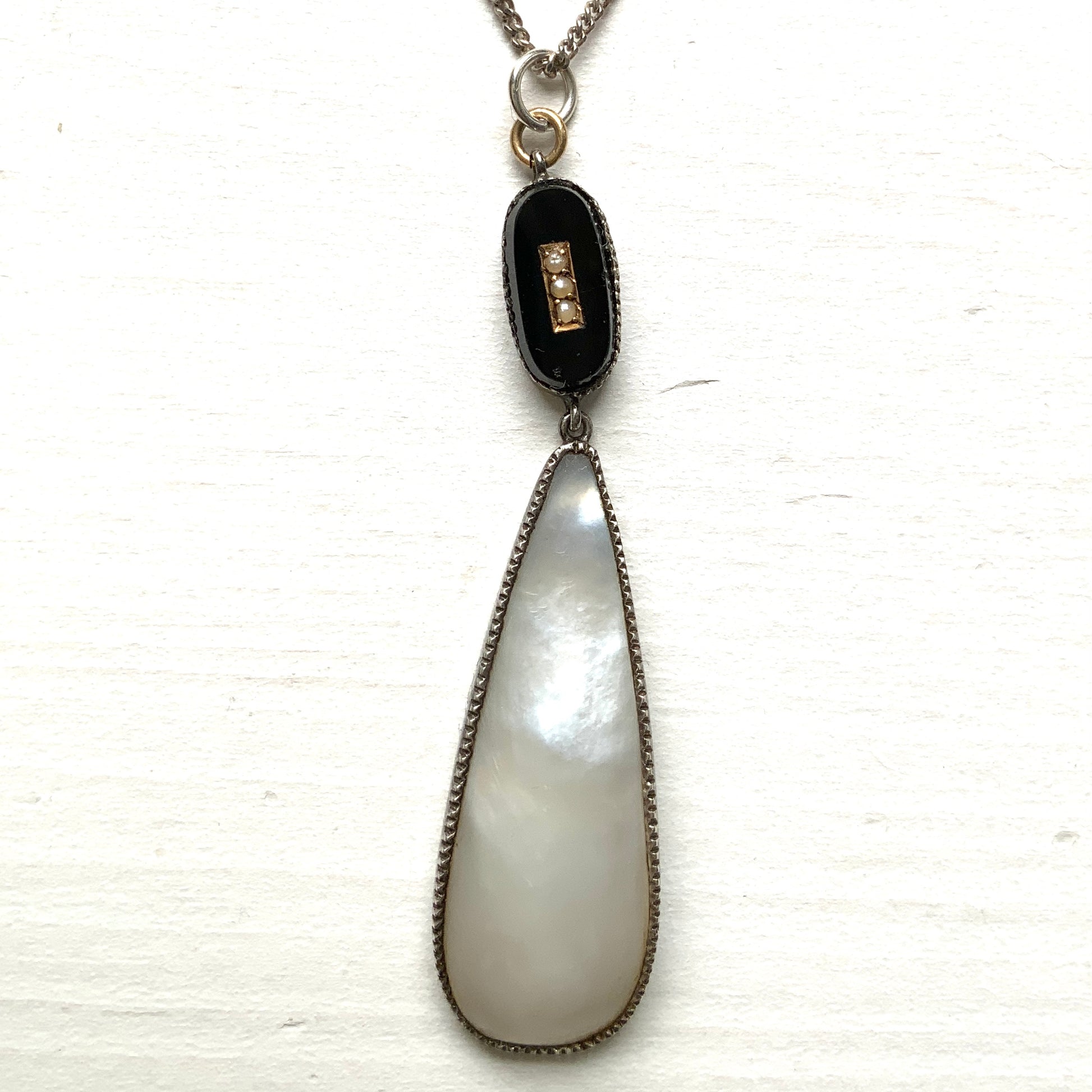 A silver necklace featuring onyx-like black glass paired with a teardrop of smooth, lustrous mother of pearl. オニキスのような艶をもつブラックグラスと、滑らかな光沢が美しいマザーオブパールのティアドロップを組み合わせた、シルバーネックレス。