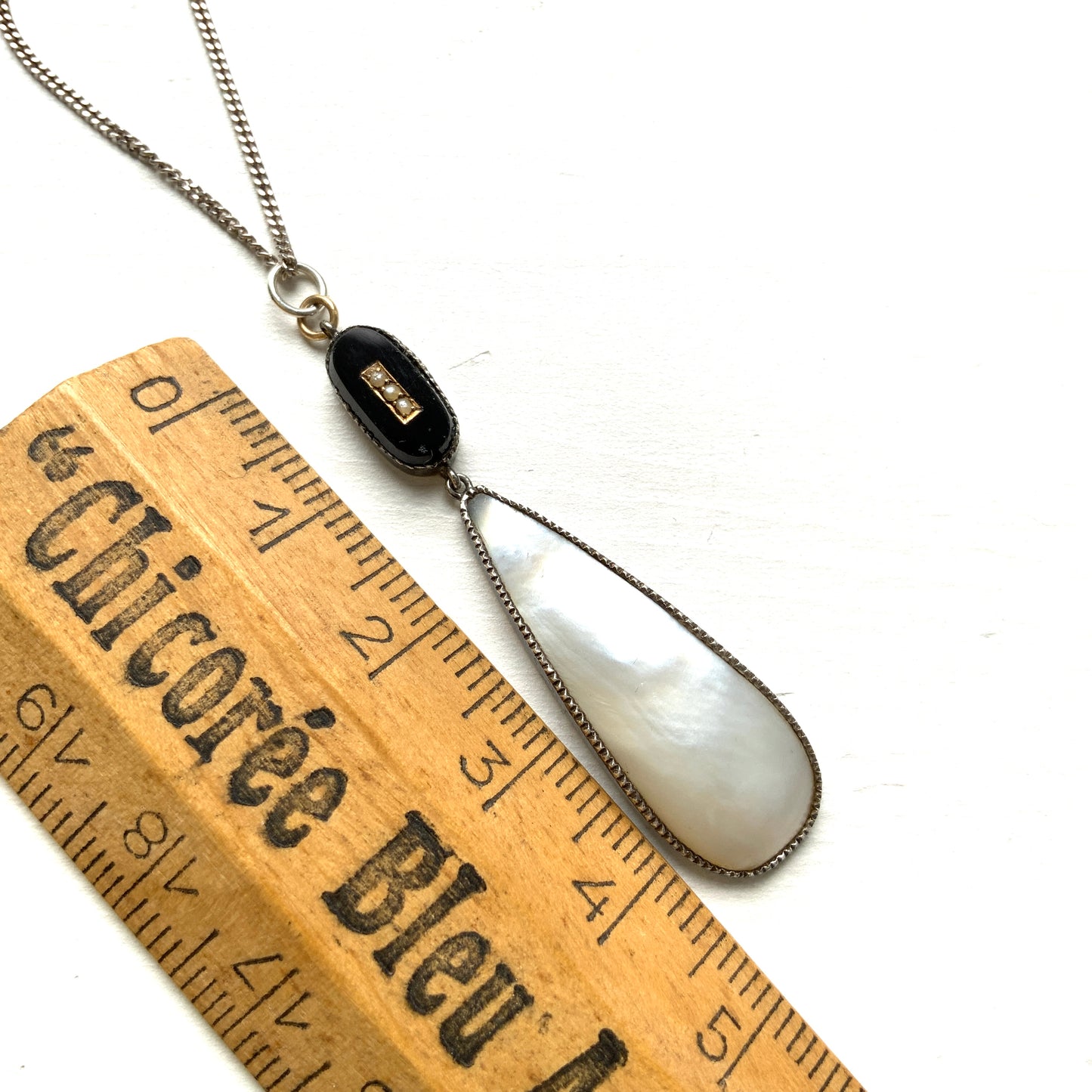 A silver necklace featuring onyx-like black glass paired with a teardrop of smooth, lustrous mother of pearl. オニキスのような艶をもつブラックグラスと、滑らかな光沢が美しいマザーオブパールのティアドロップを組み合わせた、シルバーネックレス。