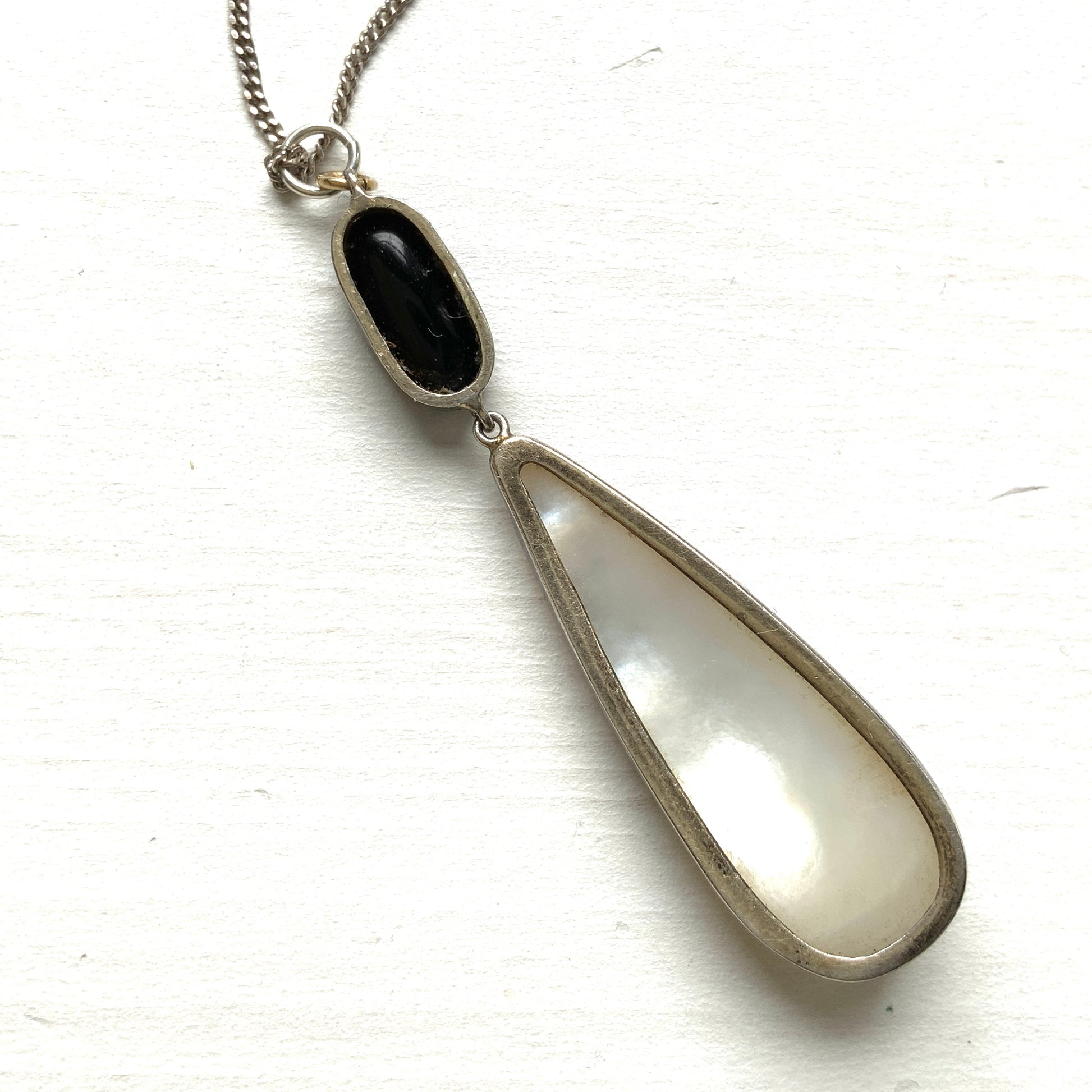A silver necklace featuring onyx-like black glass paired with a teardrop of smooth, lustrous mother of pearl. オニキスのような艶をもつブラックグラスと、滑らかな光沢が美しいマザーオブパールのティアドロップを組み合わせた、シルバーネックレス。