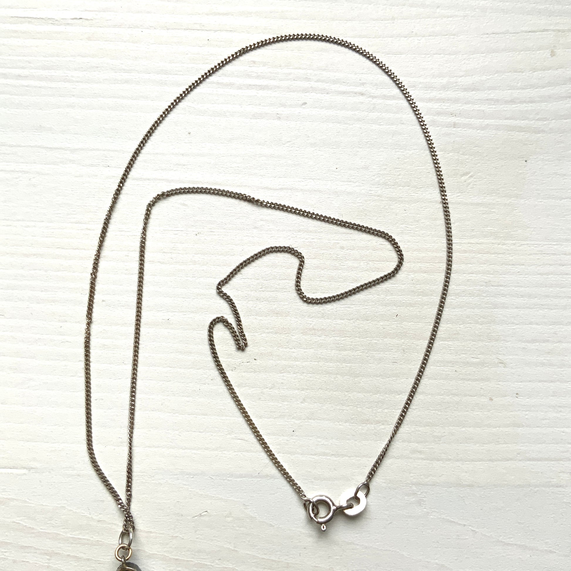 A silver necklace featuring onyx-like black glass paired with a teardrop of smooth, lustrous mother of pearl. オニキスのような艶をもつブラックグラスと、滑らかな光沢が美しいマザーオブパールのティアドロップを組み合わせた、シルバーネックレス。