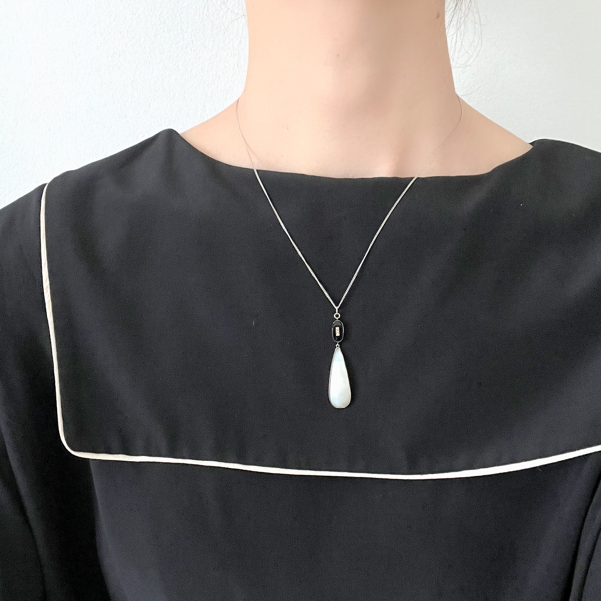 A silver necklace featuring onyx-like black glass paired with a teardrop of smooth, lustrous mother of pearl. オニキスのような艶をもつブラックグラスと、滑らかな光沢が美しいマザーオブパールのティアドロップを組み合わせた、シルバーネックレス。