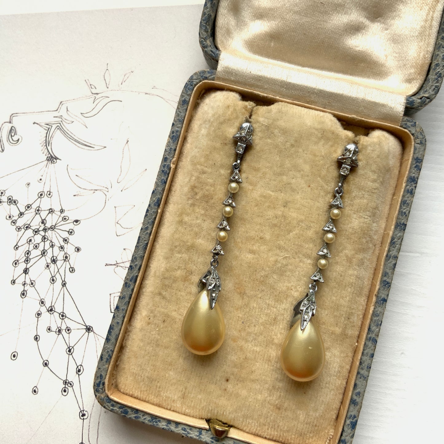 Screw earrings featuring a silver-tone leaf with a champagne gold teardrop pearl glass dangling from the tip. シルバートーンのリーフの先にシャンパンゴールドカラーのティアドロップグラスパールが揺れるスクリューイヤリング。