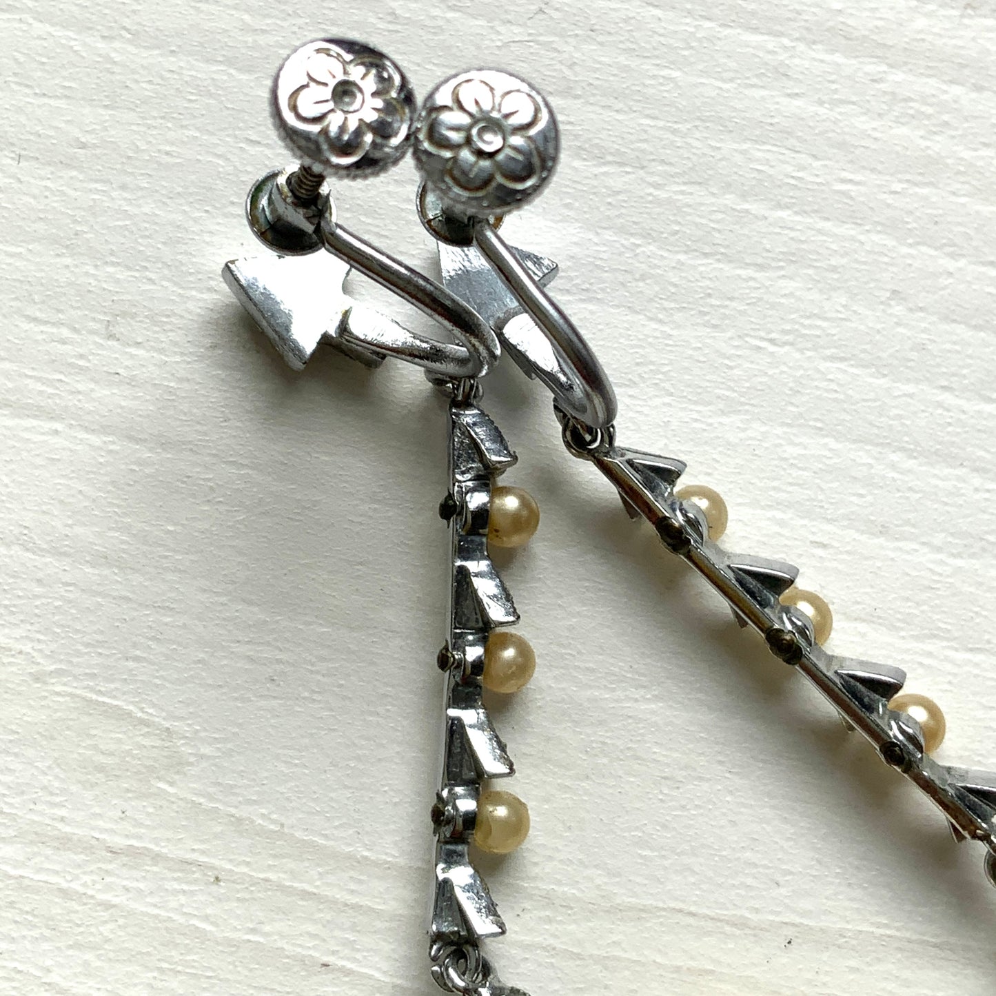 Screw earrings featuring a silver-tone leaf with a champagne gold teardrop pearl glass dangling from the tip. シルバートーンのリーフの先にシャンパンゴールドカラーのティアドロップグラスパールが揺れるスクリューイヤリング。
