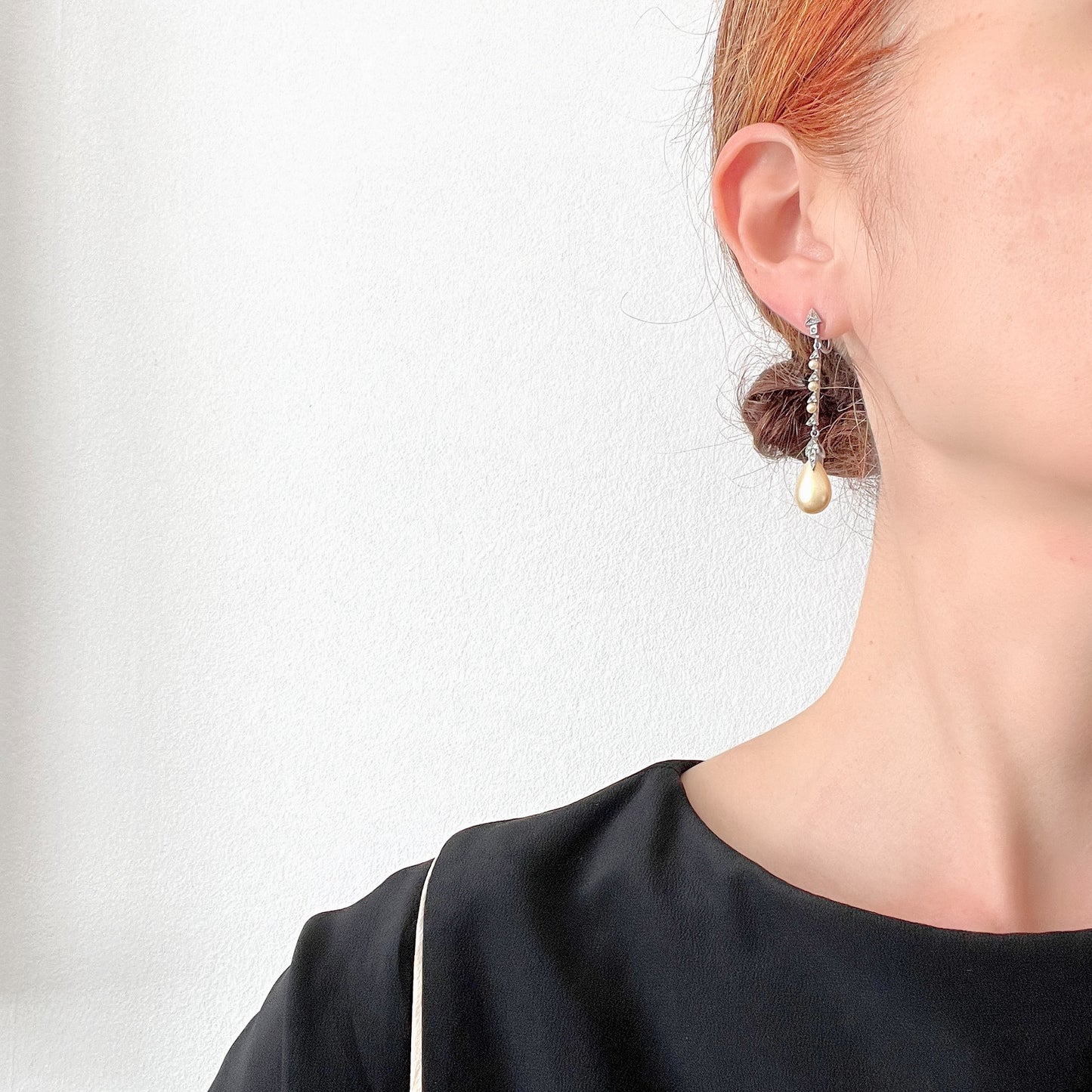 Screw earrings featuring a silver-tone leaf with a champagne gold teardrop pearl glass dangling from the tip. シルバートーンのリーフの先にシャンパンゴールドカラーのティアドロップグラスパールが揺れるスクリューイヤリング。