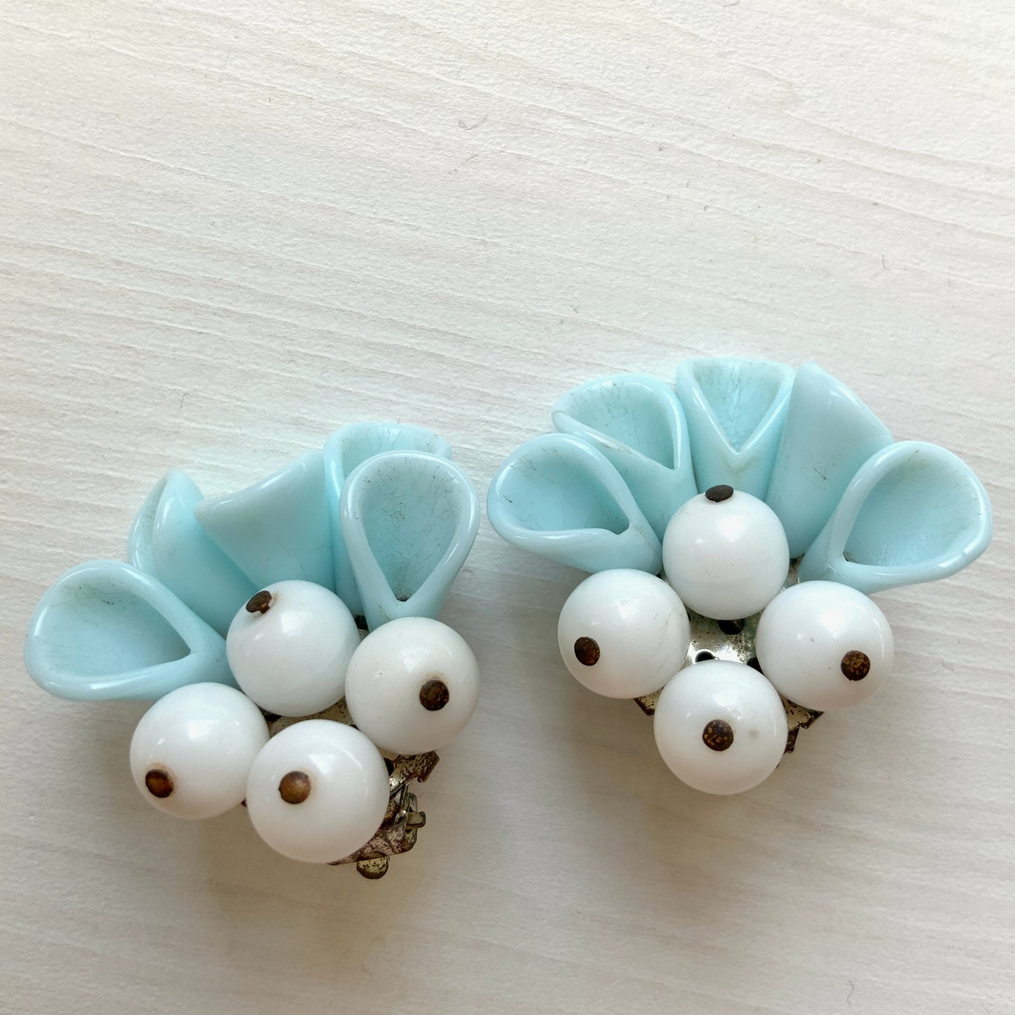 These clip-on earrings feature petal-like pastel blue glass beads paired with white milk glass beads that resemble berries. 花びらのような淡いパステルブルーのグラスビーズに、白い実のようなミルクグラスビーズがついたクリップイヤリング。