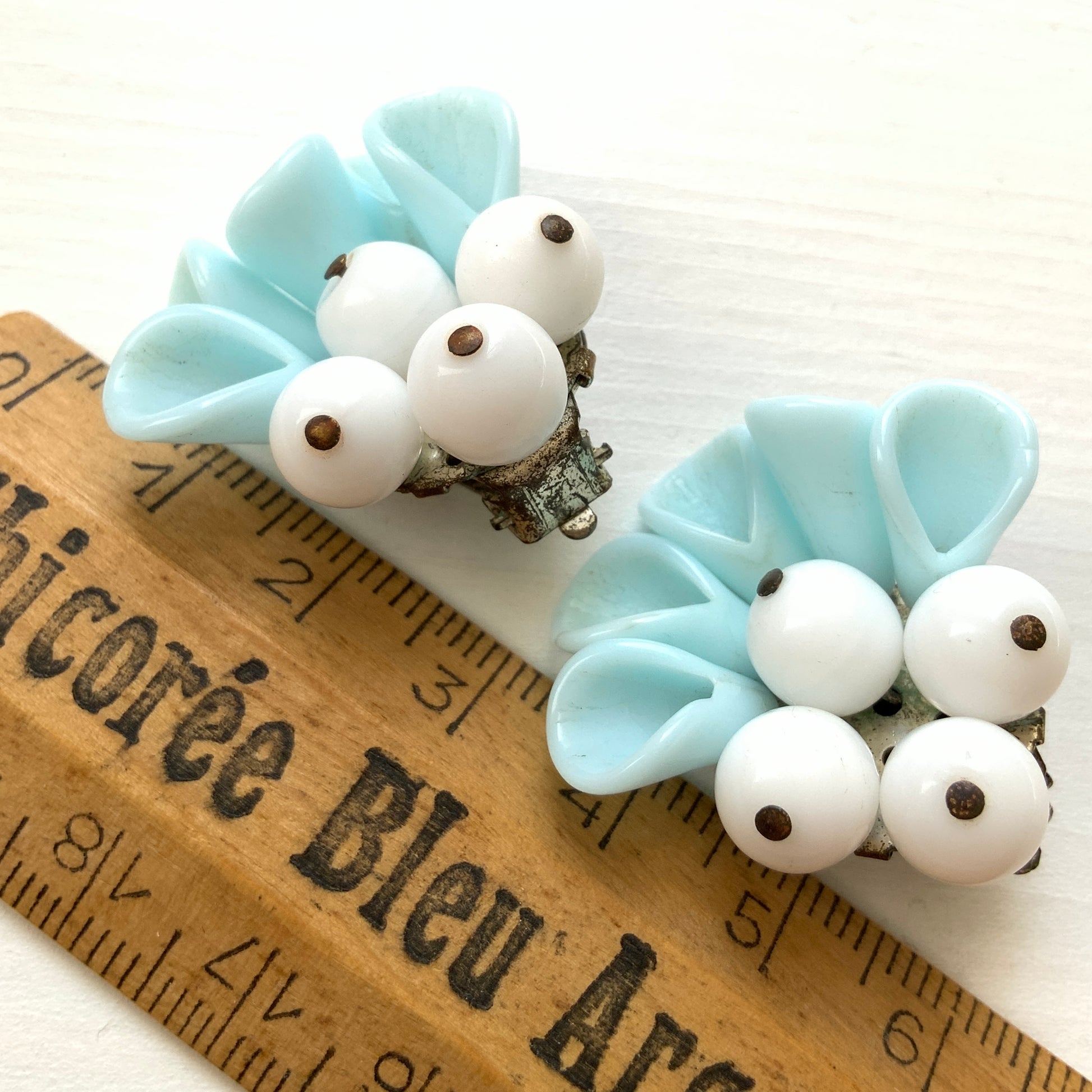 These clip-on earrings feature petal-like pastel blue glass beads paired with white milk glass beads that resemble berries. 花びらのような淡いパステルブルーのグラスビーズに、白い実のようなミルクグラスビーズがついたクリップイヤリング。