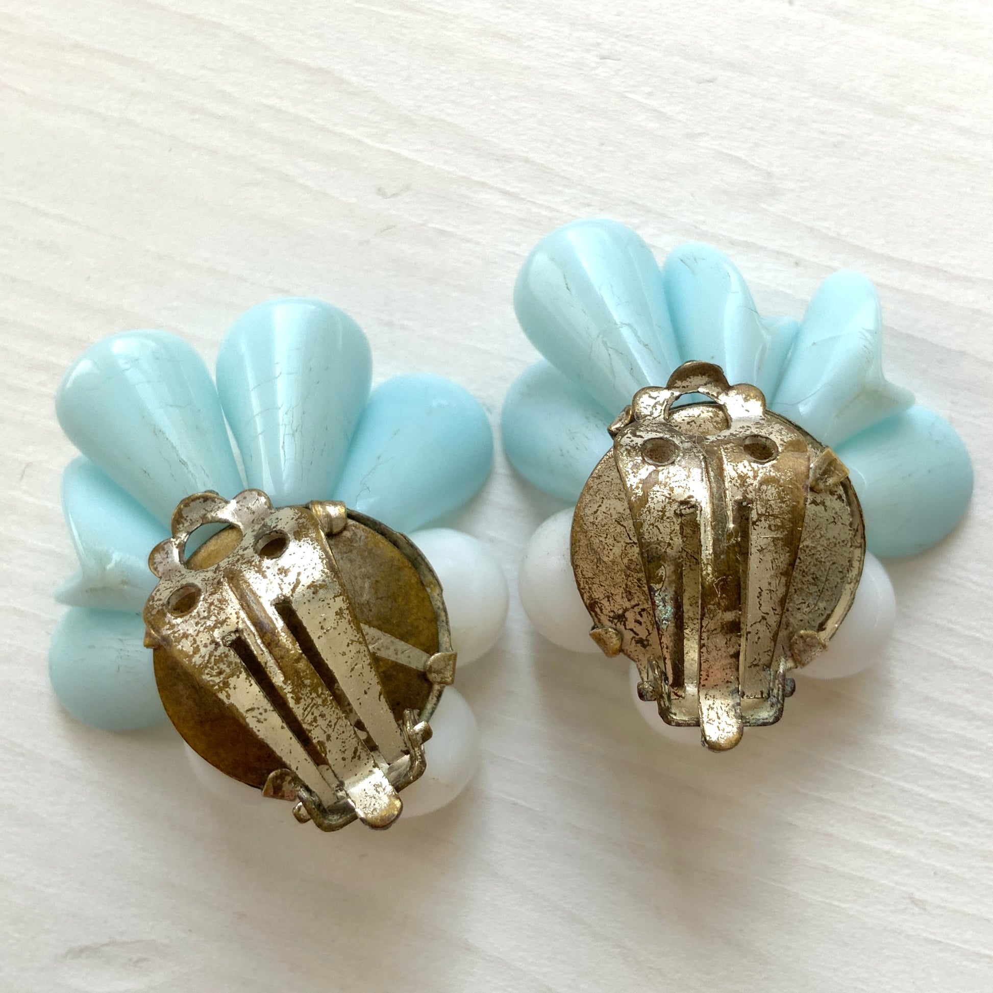 These clip-on earrings feature petal-like pastel blue glass beads paired with white milk glass beads that resemble berries. 花びらのような淡いパステルブルーのグラスビーズに、白い実のようなミルクグラスビーズがついたクリップイヤリング。