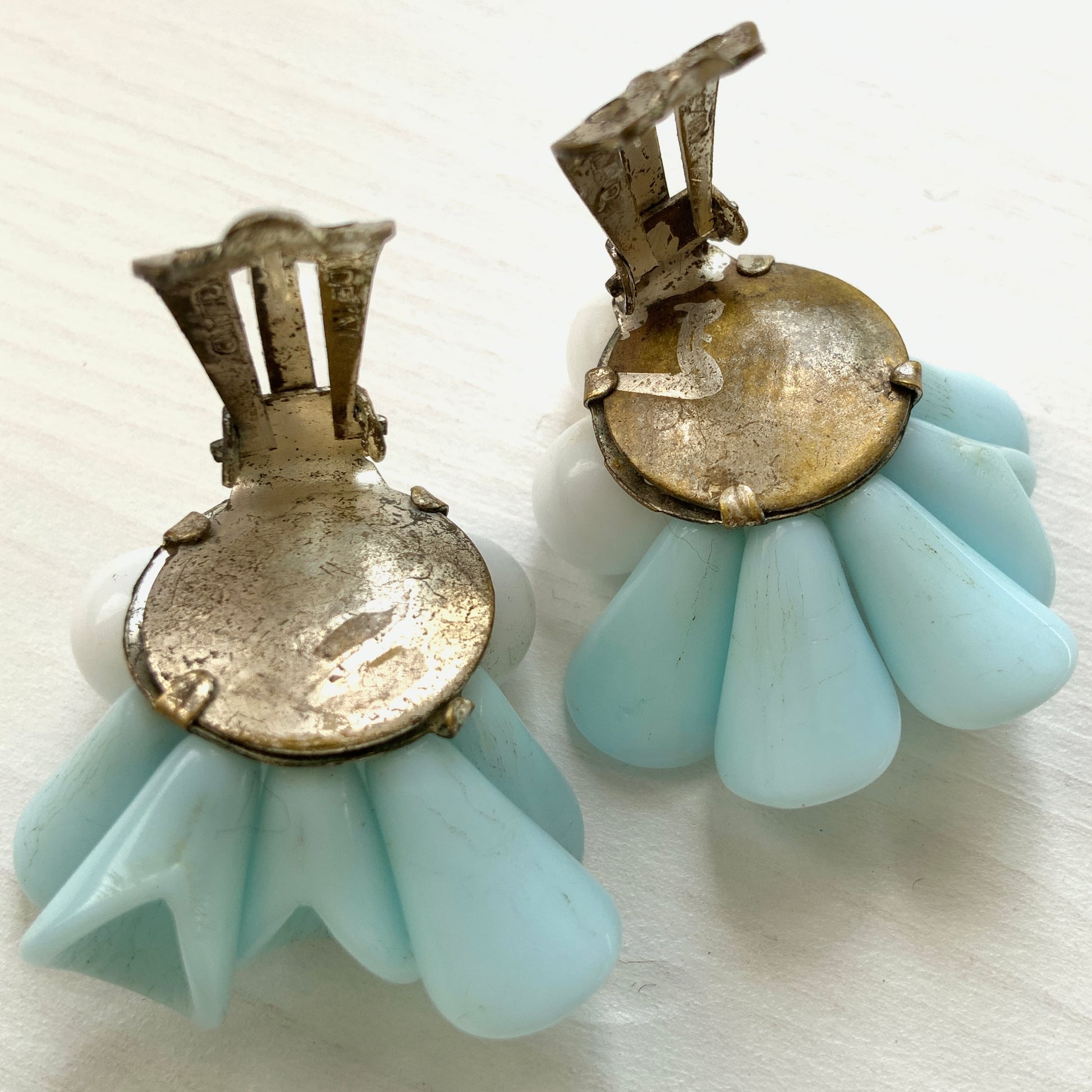 These clip-on earrings feature petal-like pastel blue glass beads paired with white milk glass beads that resemble berries. 花びらのような淡いパステルブルーのグラスビーズに、白い実のようなミルクグラスビーズがついたクリップイヤリング。