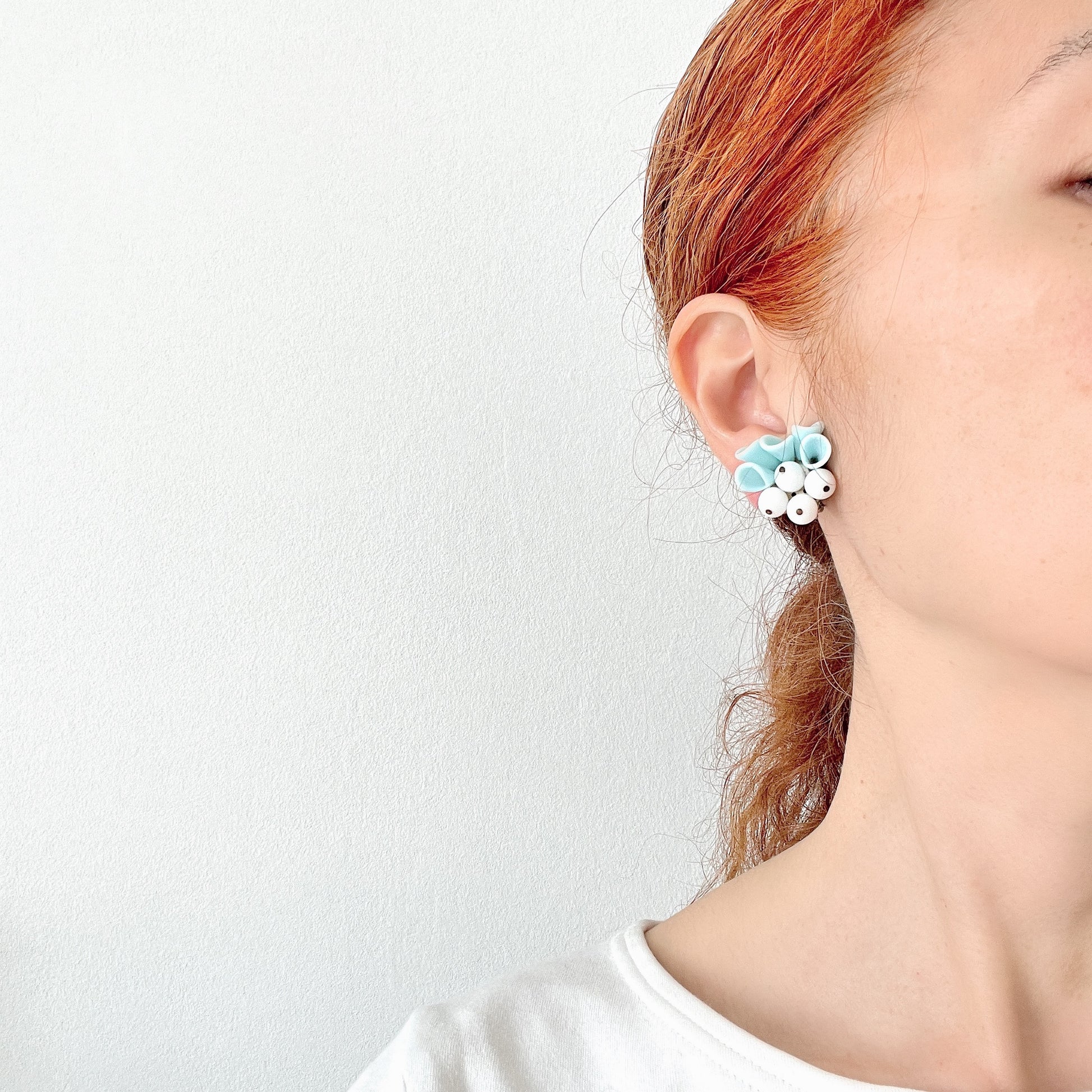 These clip-on earrings feature petal-like pastel blue glass beads paired with white milk glass beads that resemble berries. 花びらのような淡いパステルブルーのグラスビーズに、白い実のようなミルクグラスビーズがついたクリップイヤリング。