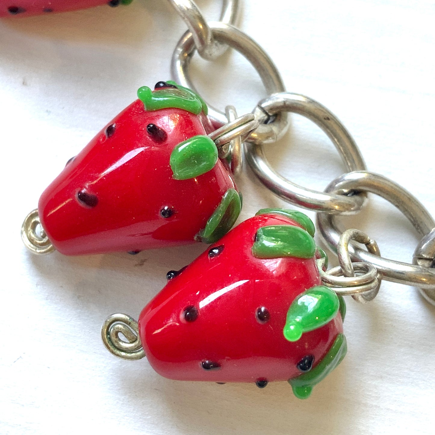 A bracelet with glass strawberry charms that sway from a silver-tone chain. ガラスのストロベリーチャームが揺れるブレスレット。