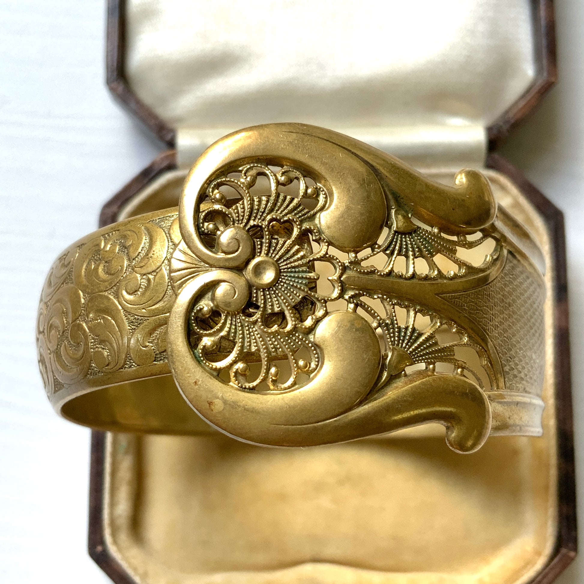 This gold-tone metal bangle features an elegant buckle adorned with delicate filigree work.  フィリグリーで装飾されたエレガントなバックルが印象的なゴールドトーンメタルのバングル。