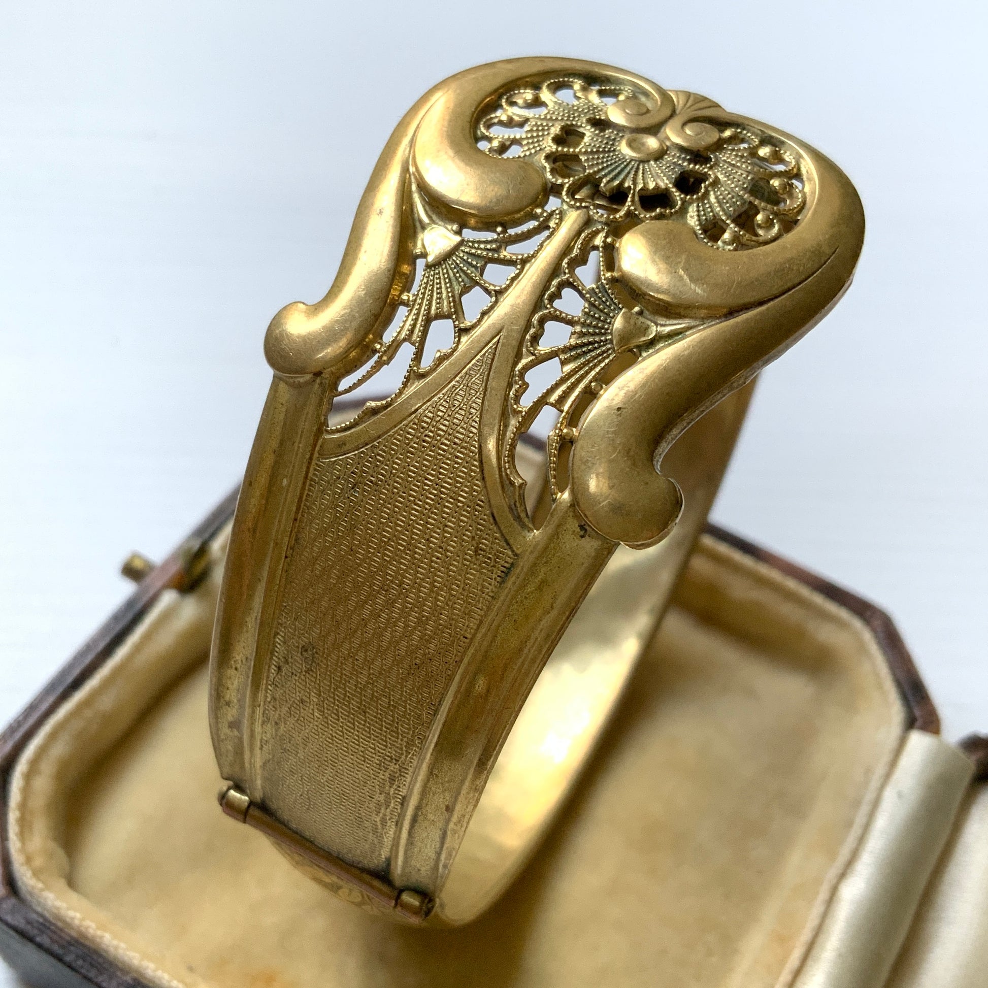 This gold-tone metal bangle features an elegant buckle adorned with delicate filigree work.  フィリグリーで装飾されたエレガントなバックルが印象的なゴールドトーンメタルのバングル。
