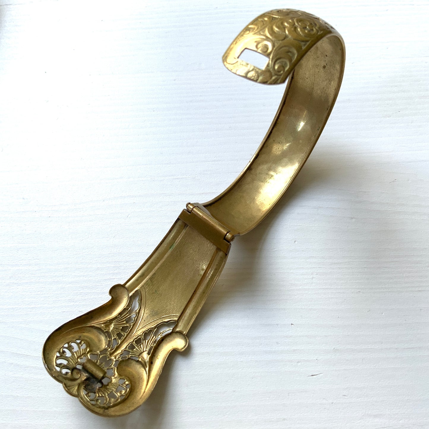 This gold-tone metal bangle features an elegant buckle adorned with delicate filigree work.  フィリグリーで装飾されたエレガントなバックルが印象的なゴールドトーンメタルのバングル。