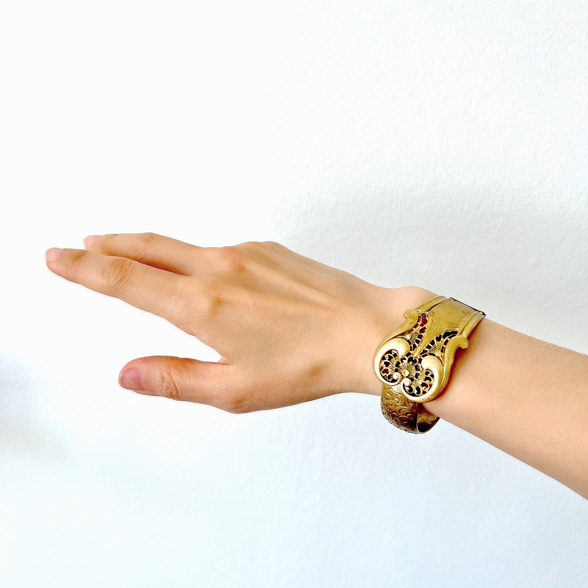This gold-tone metal bangle features an elegant buckle adorned with delicate filigree work.  フィリグリーで装飾されたエレガントなバックルが印象的なゴールドトーンメタルのバングル。