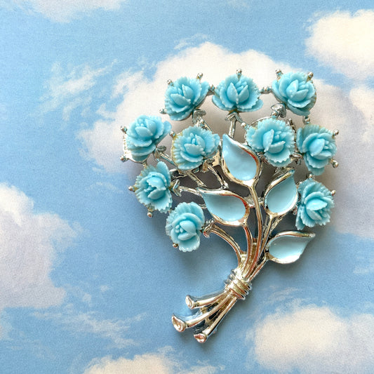 A bouquet brooch featuring sky blue plastic roses, with matching enamel-coated leaves and silver-tone branches that beautifully complement the color scheme. 空色のプラスチックのバラのブーケブローチ。