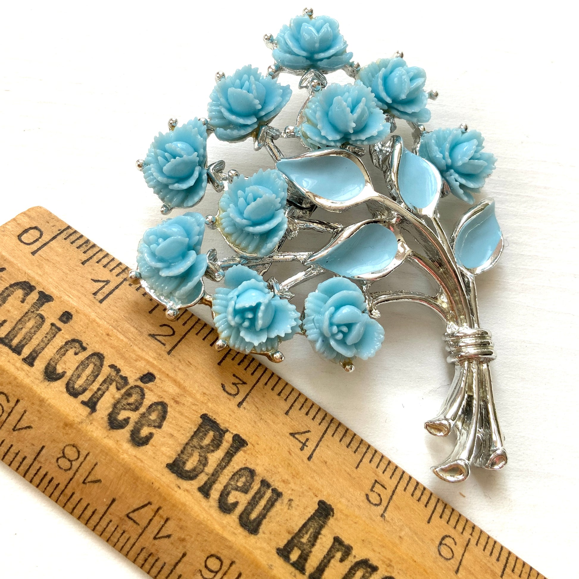 A bouquet brooch featuring sky blue plastic roses, with matching enamel-coated leaves and silver-tone branches that beautifully complement the color scheme. 空色のプラスチックのバラのブーケブローチ。