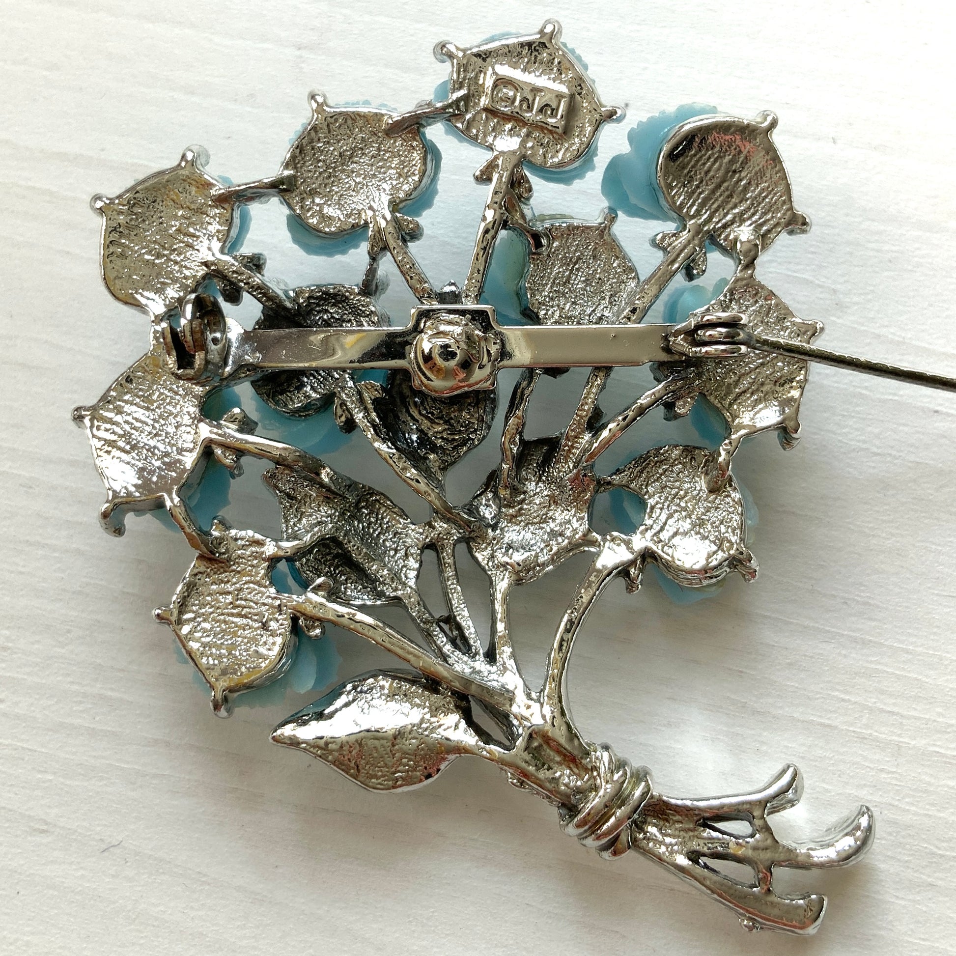A bouquet brooch featuring sky blue plastic roses, with matching enamel-coated leaves and silver-tone branches that beautifully complement the color scheme. 空色のプラスチックのバラのブーケブローチ。