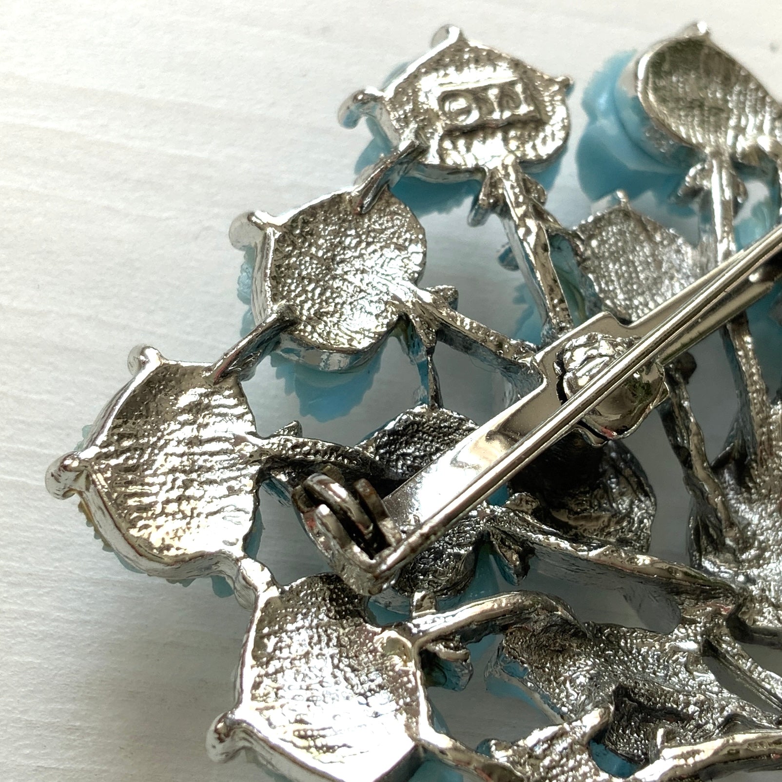 A bouquet brooch featuring sky blue plastic roses, with matching enamel-coated leaves and silver-tone branches that beautifully complement the color scheme. 空色のプラスチックのバラのブーケブローチ。