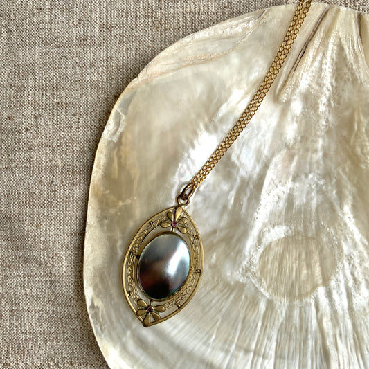 A pendant necklace featuring a large silver-coloured mabe pearl and gold-tone filigree.  大きなシルバーカラーのマベパール と、ゴールドトーンのフィリグリーのペンダントネックレス。