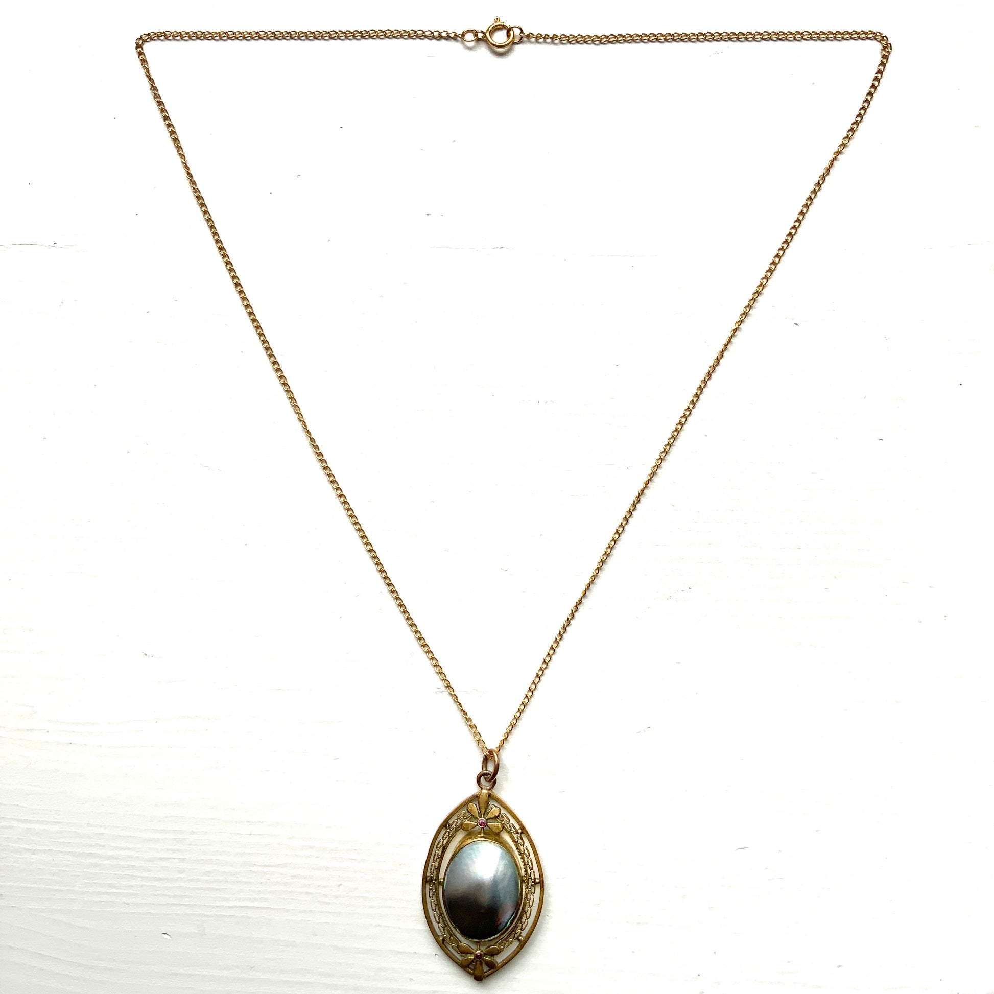 A pendant necklace featuring a large silver-coloured mabe pearl and gold-tone filigree.  大きなシルバーカラーのマベパール と、ゴールドトーンのフィリグリーのペンダントネックレス。