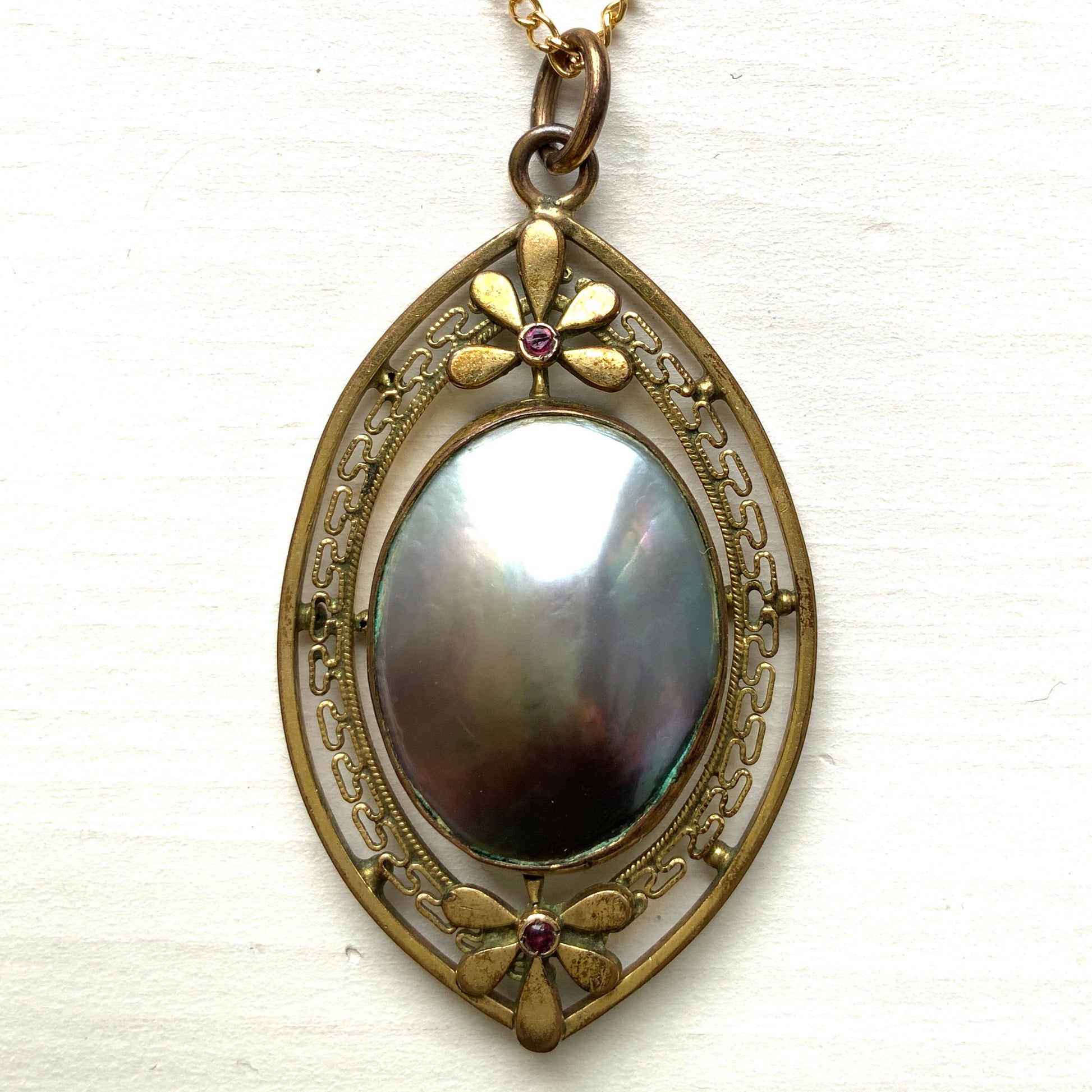 A pendant necklace featuring a large silver-coloured mabe pearl and gold-tone filigree.  大きなシルバーカラーのマベパール と、ゴールドトーンのフィリグリーのペンダントネックレス。