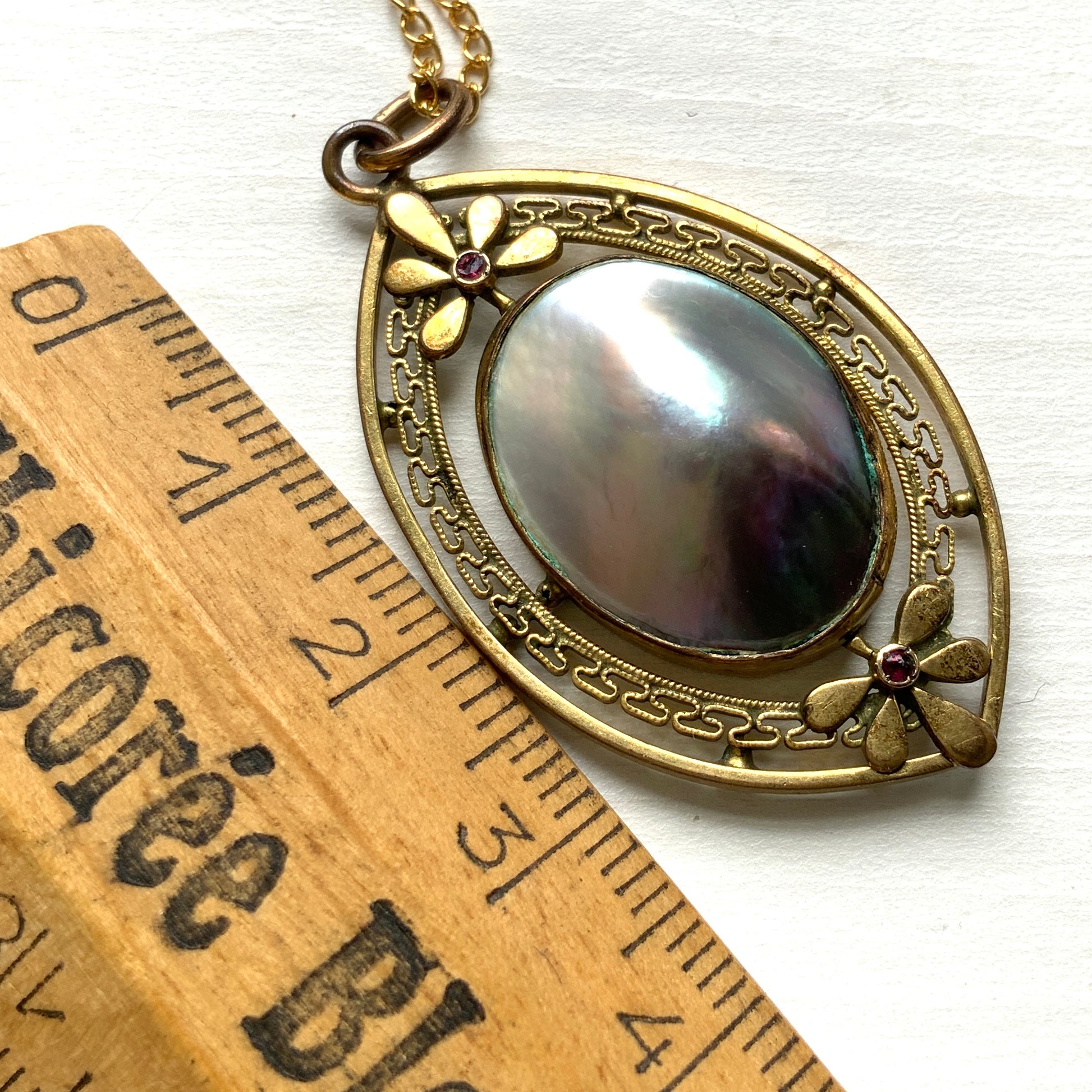 A pendant necklace featuring a large silver-coloured mabe pearl and gold-tone filigree.  大きなシルバーカラーのマベパール と、ゴールドトーンのフィリグリーのペンダントネックレス。