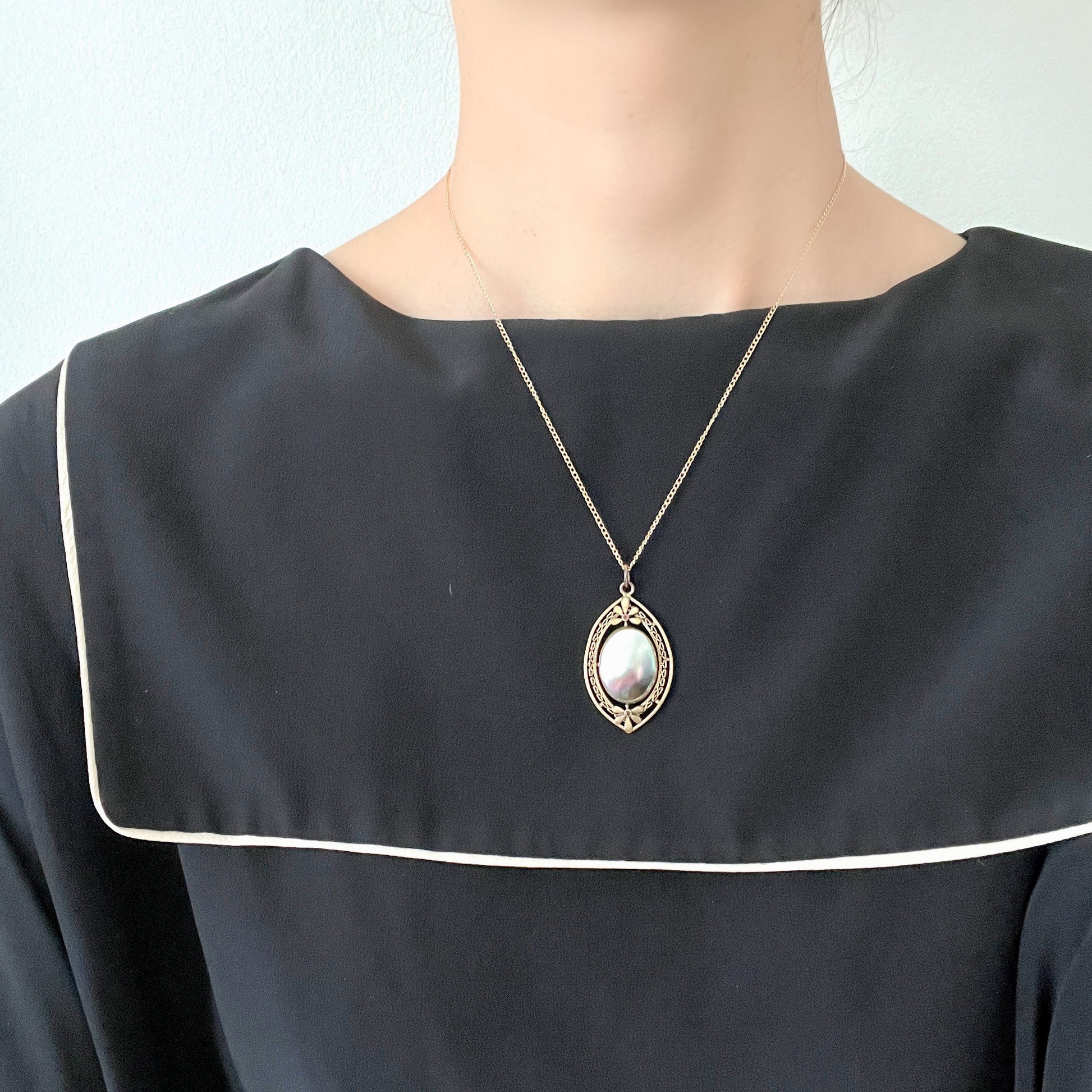 A pendant necklace featuring a large silver-coloured mabe pearl and gold-tone filigree.  大きなシルバーカラーのマベパール と、ゴールドトーンのフィリグリーのペンダントネックレス。