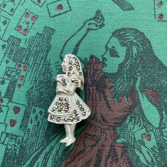 A silver brooch featuring Alice from Alice’s Adventures in Wonderland, adorned with sparkling marcasites.  マーカサイトが散りばめられた、不思議の国のアリスのシルバーブローチ