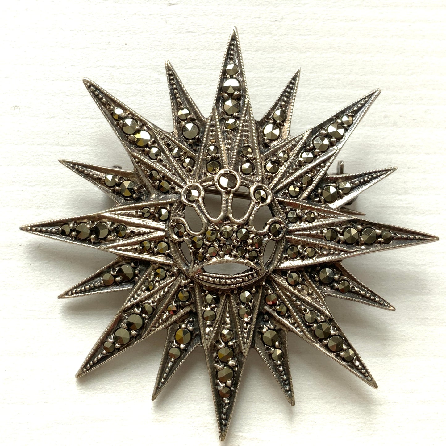 A silver brooch featuring a small crown at the centre of a starburst design. スターバーストの中央に小さな王冠があしらわれた、シルバー製のブローチ。