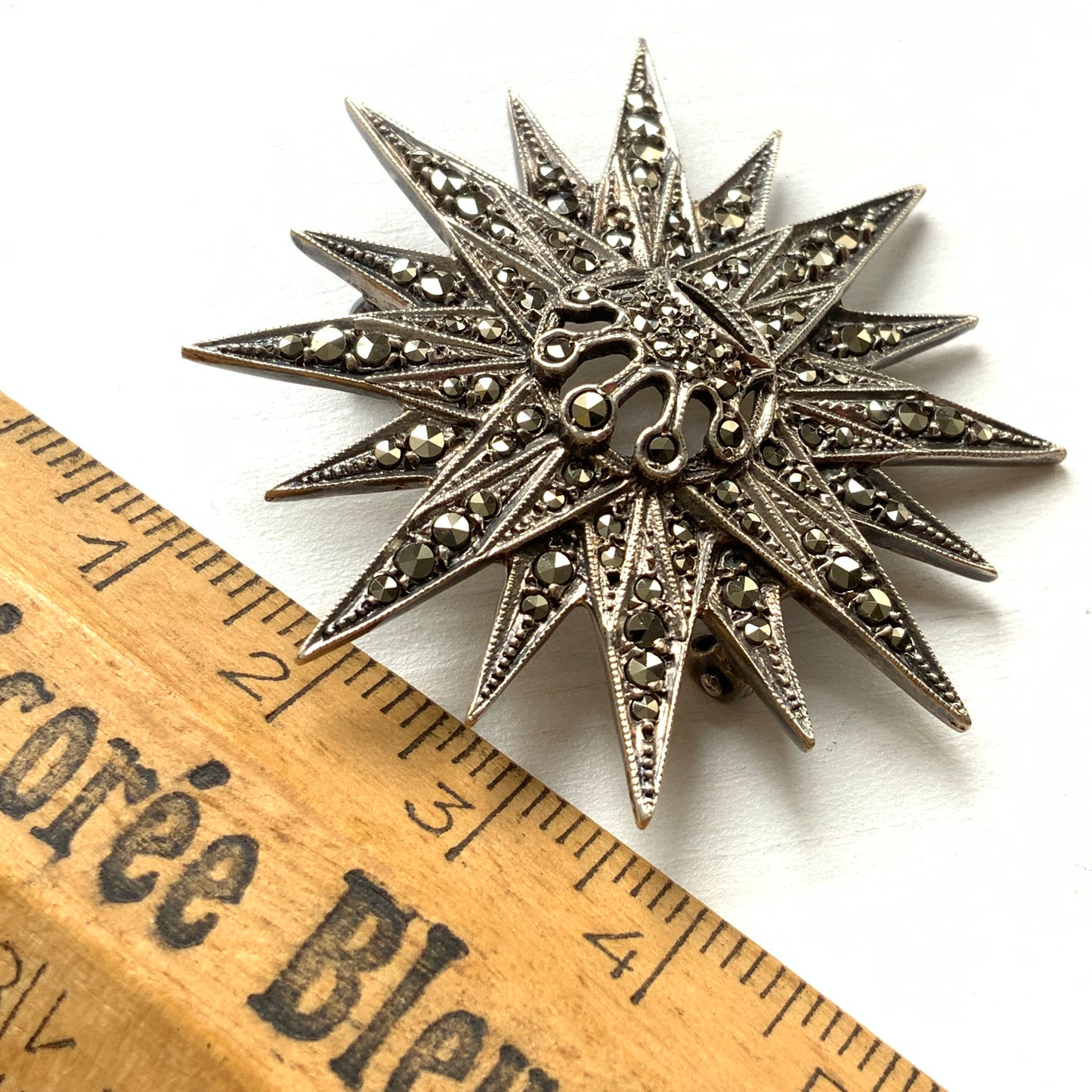 A silver brooch featuring a small crown at the centre of a starburst design. スターバーストの中央に小さな王冠があしらわれた、シルバー製のブローチ。