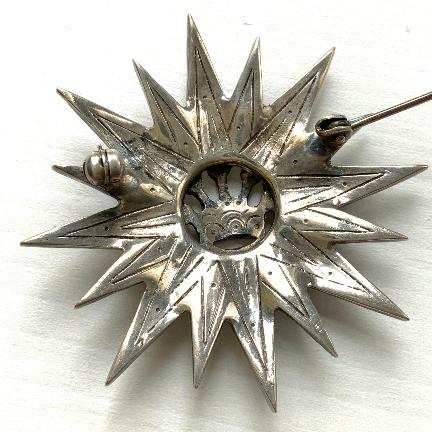 A silver brooch featuring a small crown at the centre of a starburst design. スターバーストの中央に小さな王冠があしらわれた、シルバー製のブローチ。