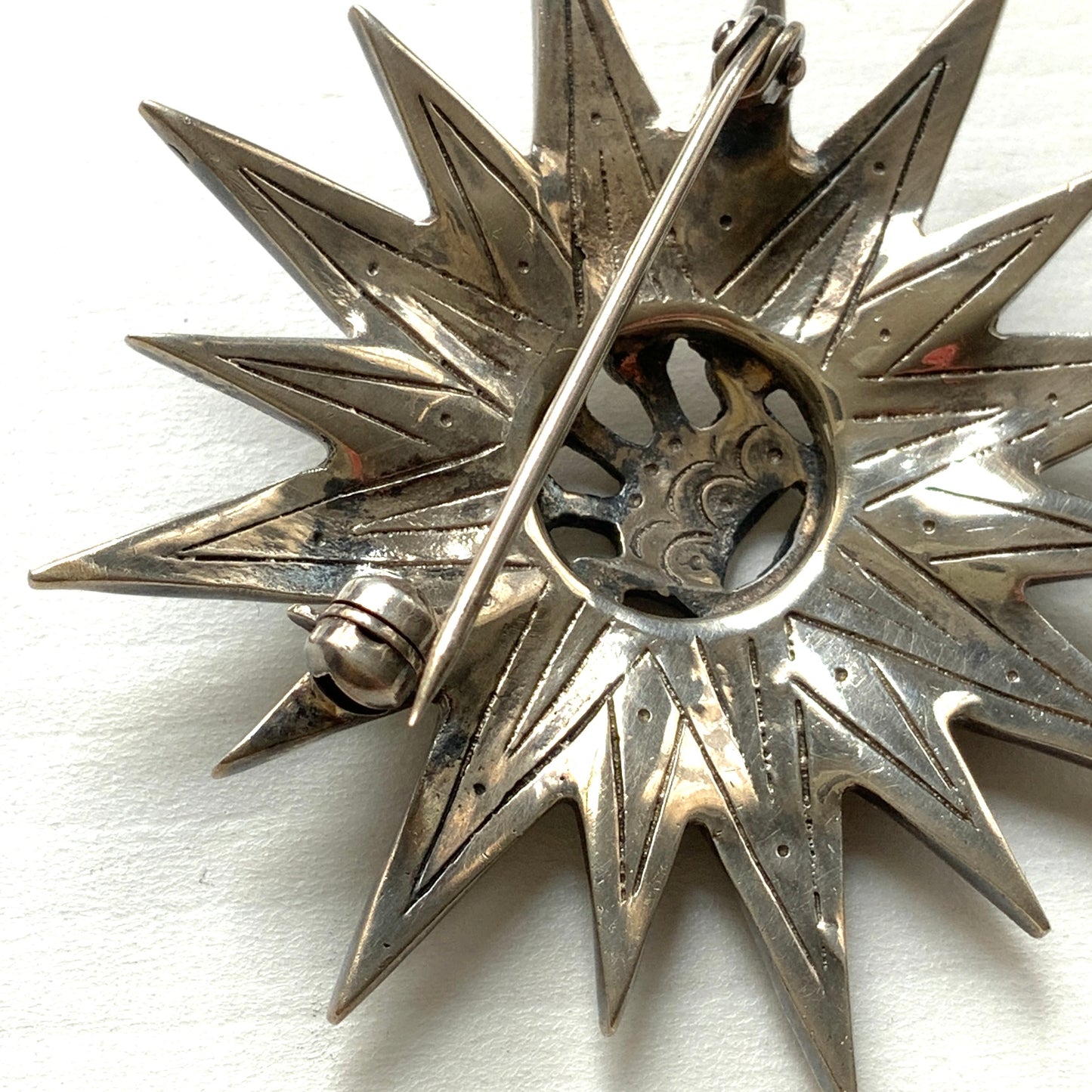 A silver brooch featuring a small crown at the centre of a starburst design. スターバーストの中央に小さな王冠があしらわれた、シルバー製のブローチ。