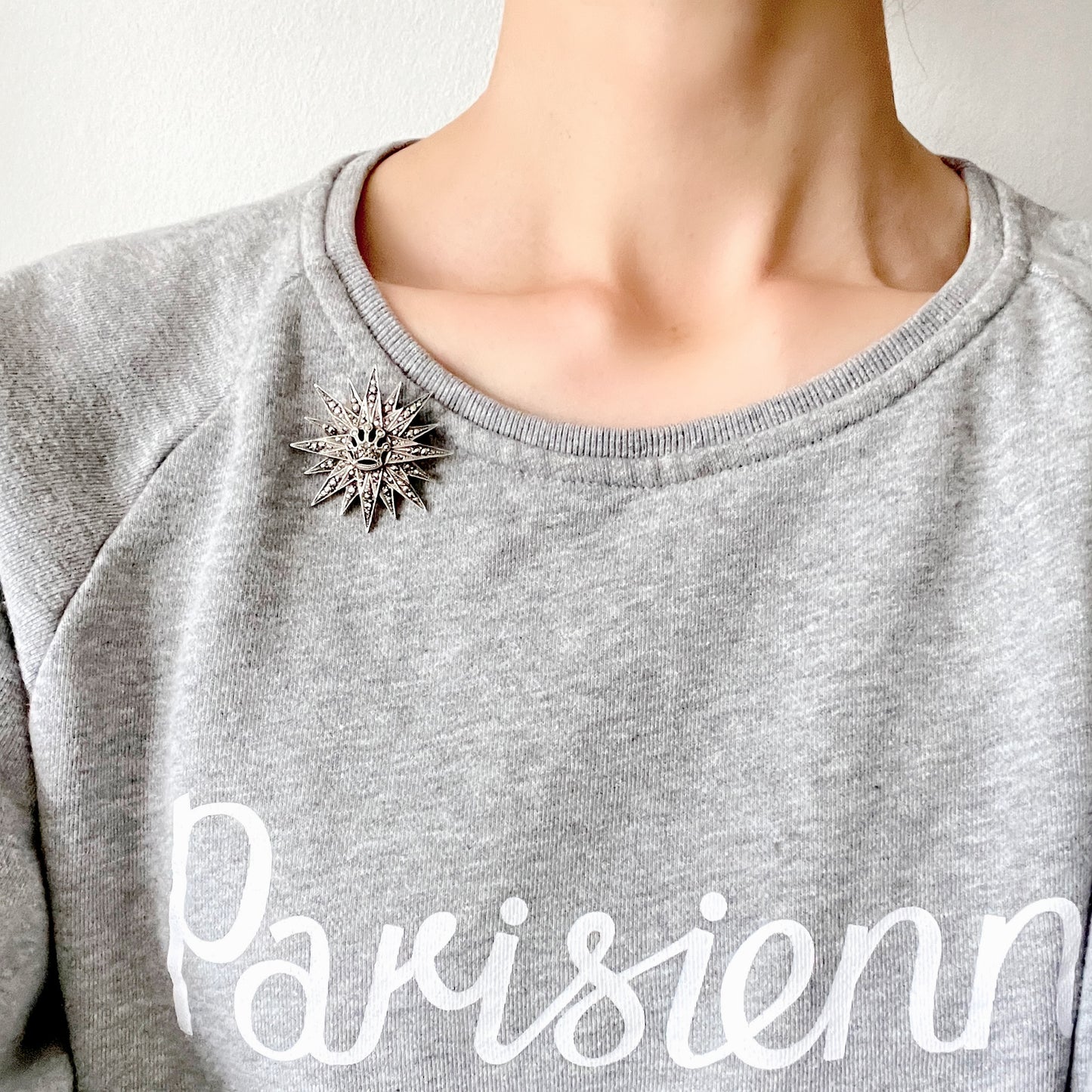 A silver brooch featuring a small crown at the centre of a starburst design. スターバーストの中央に小さな王冠があしらわれた、シルバー製のブローチ。