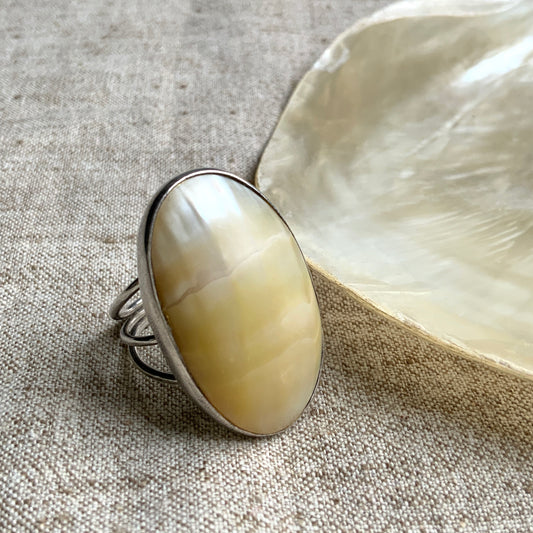 A silver ring featuring an oval domed piece of ivory-colored mother of pearl. アイボリーカラーのマザーオブパールをあしらった、オーバル型ドームのシルバーリング。