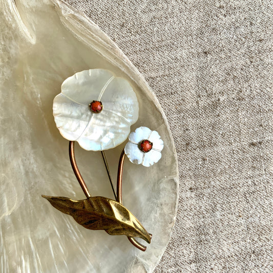 A charming brooch featuring a delicate mother of pearl flower with a soft, natural design accented by a touch of pink coral. サンゴのピンクがアクセントになった、素朴で可愛らしいデザインのマザーオブパールのお花のブローチ。