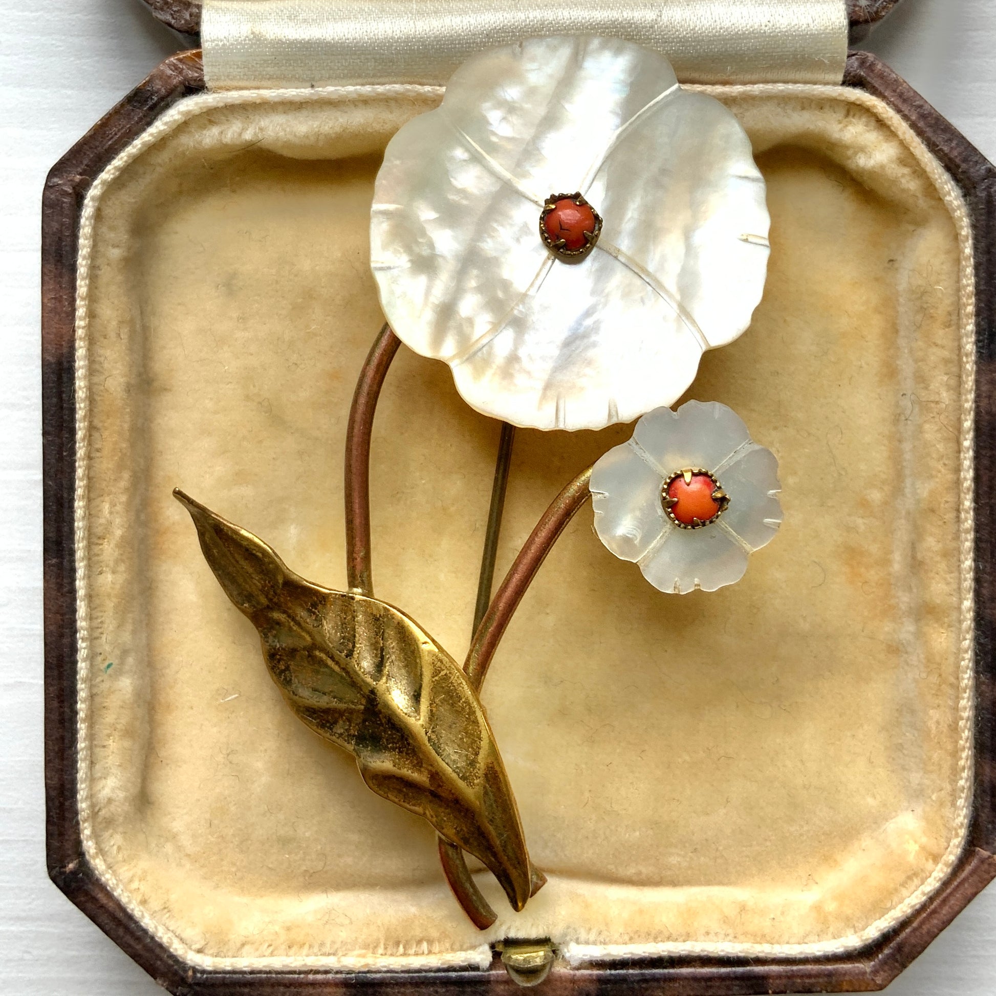 A charming brooch featuring a delicate mother of pearl flower with a soft, natural design accented by a touch of pink coral. サンゴのピンクがアクセントになった、素朴で可愛らしいデザインのマザーオブパールのお花のブローチ。