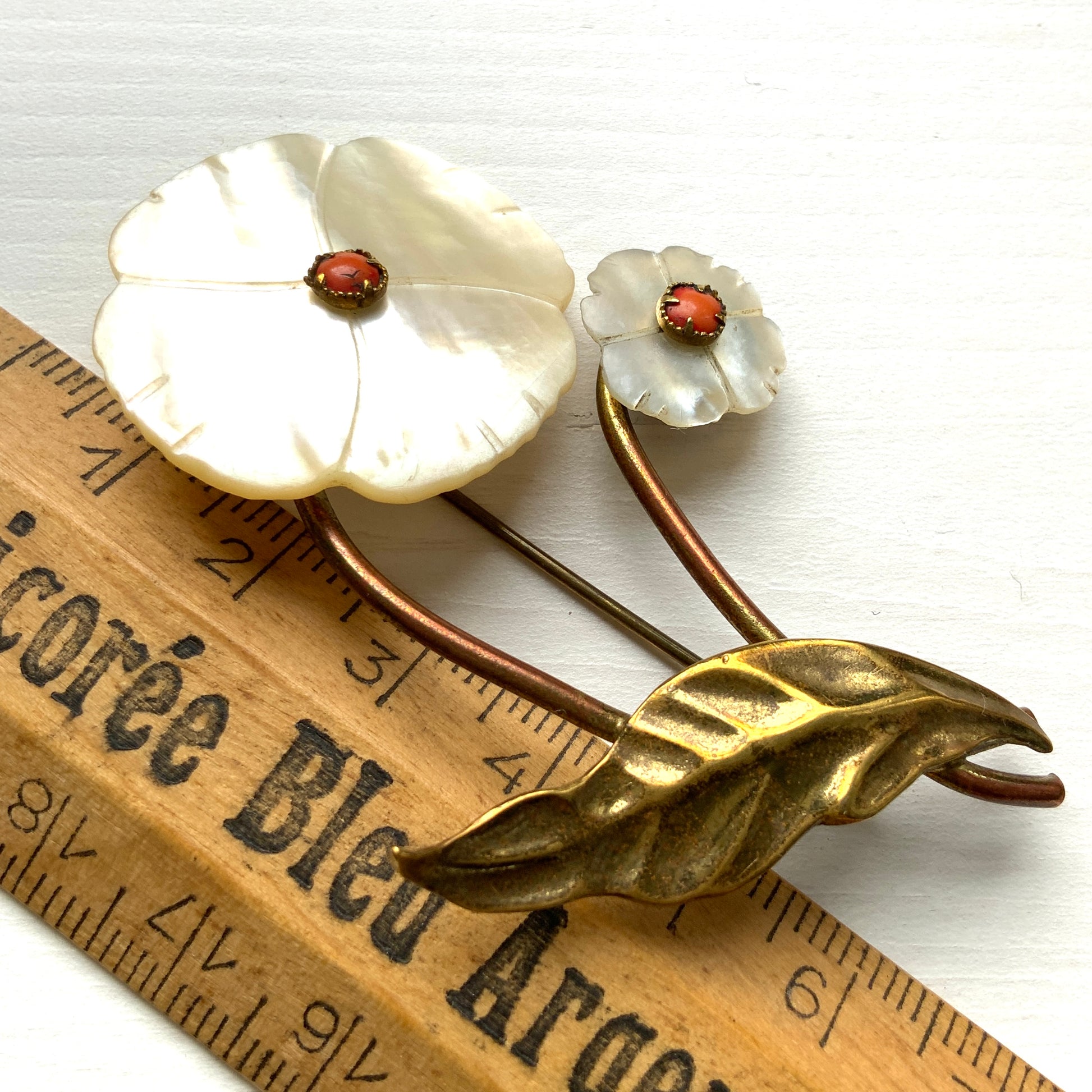 A charming brooch featuring a delicate mother of pearl flower with a soft, natural design accented by a touch of pink coral. サンゴのピンクがアクセントになった、素朴で可愛らしいデザインのマザーオブパールのお花のブローチ。