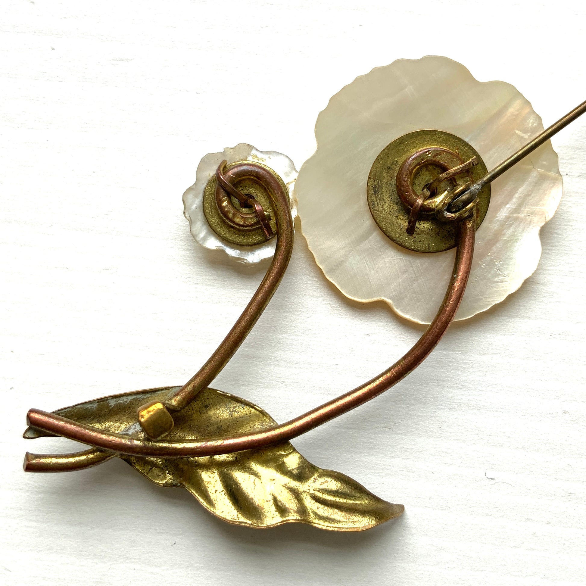 A charming brooch featuring a delicate mother of pearl flower with a soft, natural design accented by a touch of pink coral. サンゴのピンクがアクセントになった、素朴で可愛らしいデザインのマザーオブパールのお花のブローチ。