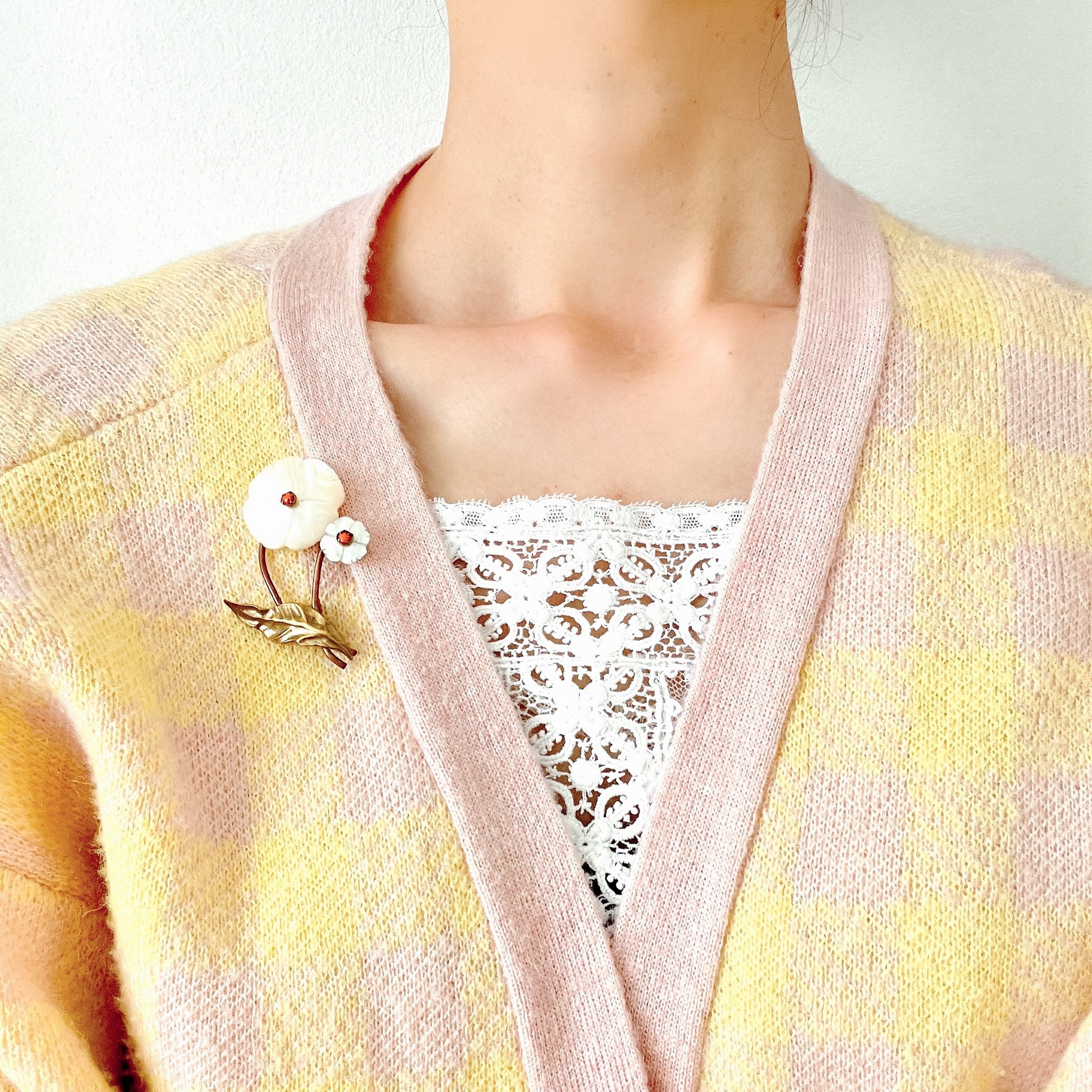 A charming brooch featuring a delicate mother of pearl flower with a soft, natural design accented by a touch of pink coral. サンゴのピンクがアクセントになった、素朴で可愛らしいデザインのマザーオブパールのお花のブローチ。
