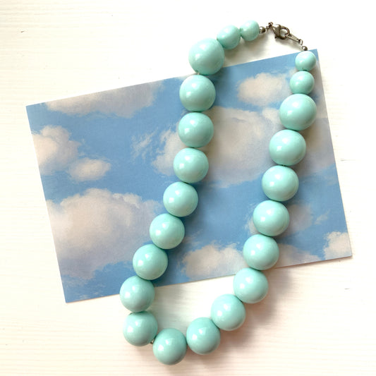 A choker necklace with large ice blue plastic beads, adding a subtle pop of cool color around the neck.  さわやかなアイスブルーのプラスチックビーズ のチョーカーネックレス。