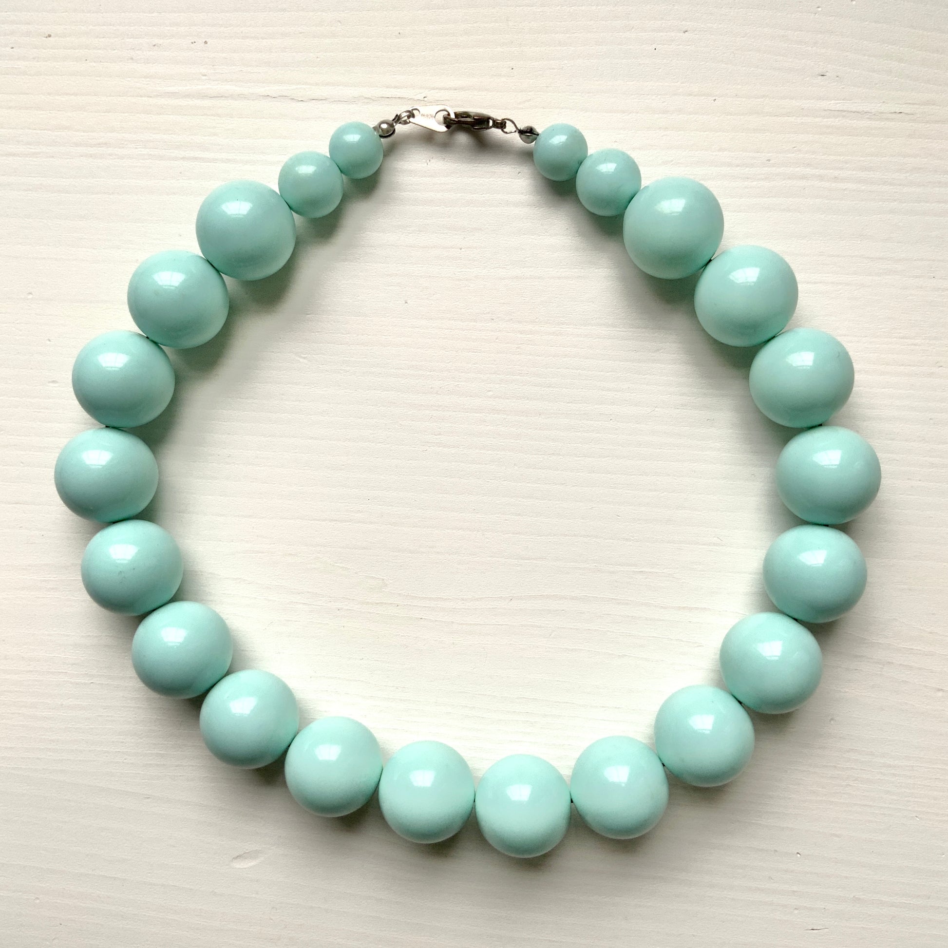 A choker necklace with large ice blue plastic beads, adding a subtle pop of cool color around the neck.  さわやかなアイスブルーのプラスチックビーズ のチョーカーネックレス。