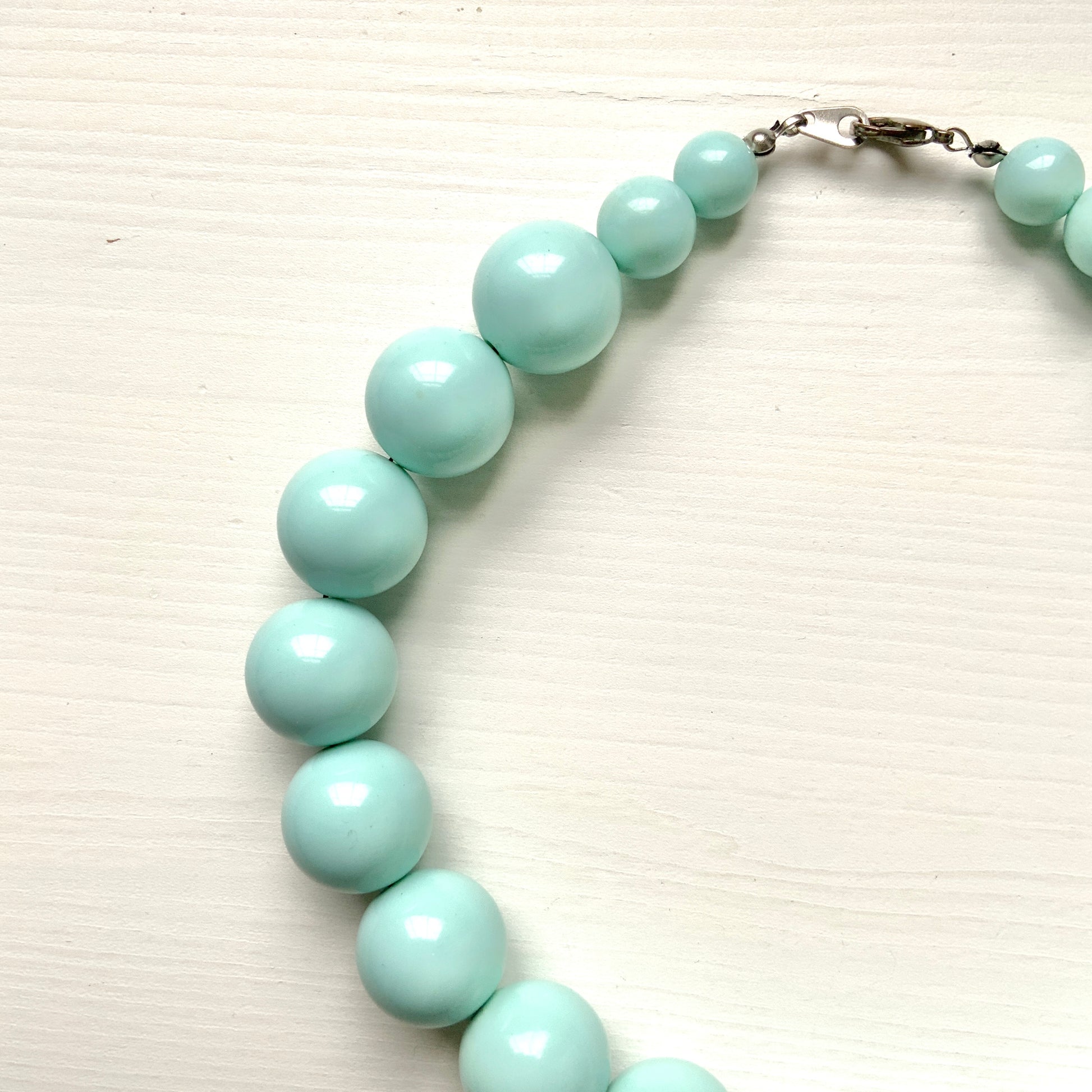 A choker necklace with large ice blue plastic beads, adding a subtle pop of cool color around the neck.  さわやかなアイスブルーのプラスチックビーズ のチョーカーネックレス。