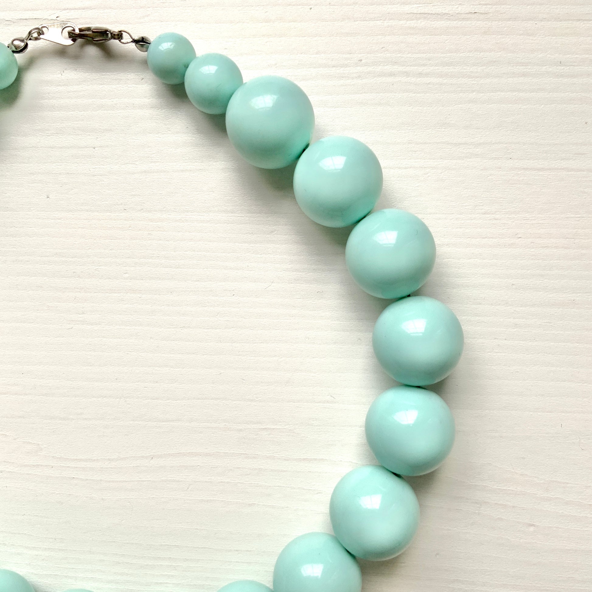 A choker necklace with large ice blue plastic beads, adding a subtle pop of cool color around the neck.  さわやかなアイスブルーのプラスチックビーズ のチョーカーネックレス。