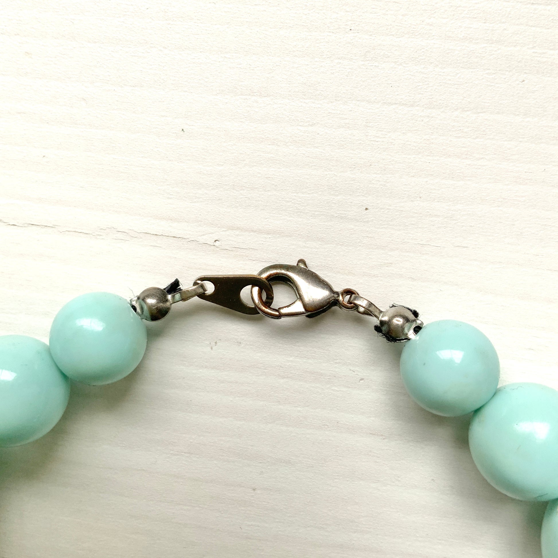 A choker necklace with large ice blue plastic beads, adding a subtle pop of cool color around the neck.  さわやかなアイスブルーのプラスチックビーズ のチョーカーネックレス。